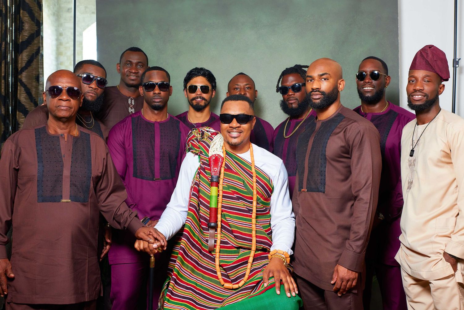 A large group wearing African traditional attire and sunglasses poses together for a formal event photo.
