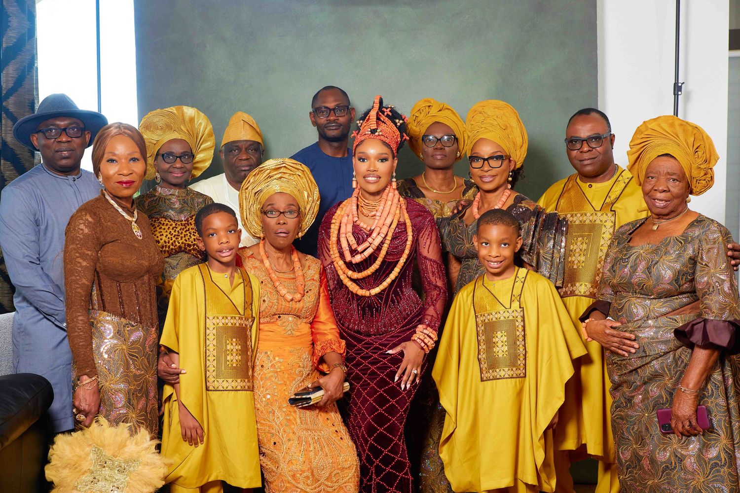Traditional West African wedding party posing together wearing vibrant yellow, orange and burgundy attire.