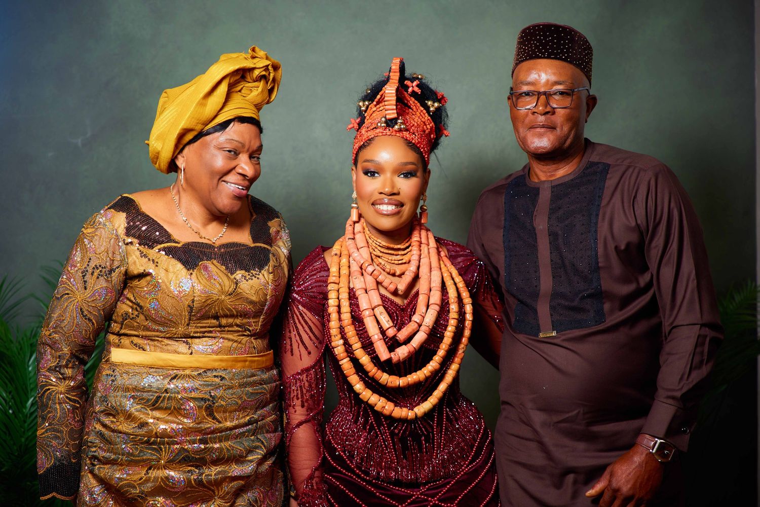 People in traditional West African attire pose together wearing vibrant coral beads and elegant formal clothing.