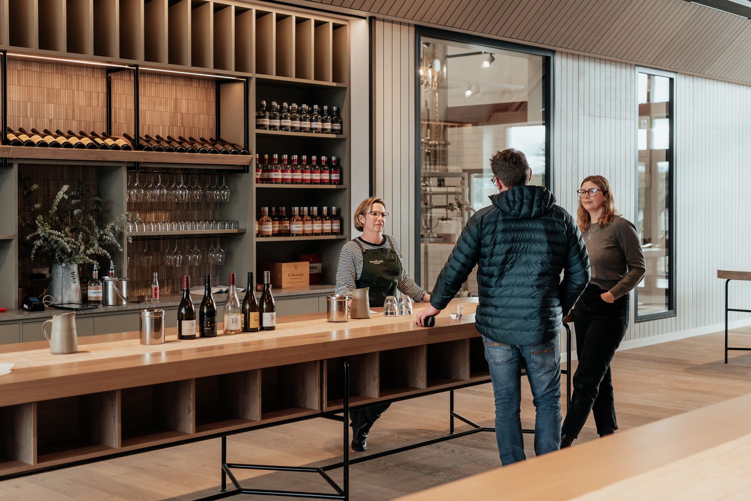 Modern cellar door at The Runholder features sleek wooden shelving, minimal design, and a couple enjoying a wine tasting by August & Vine