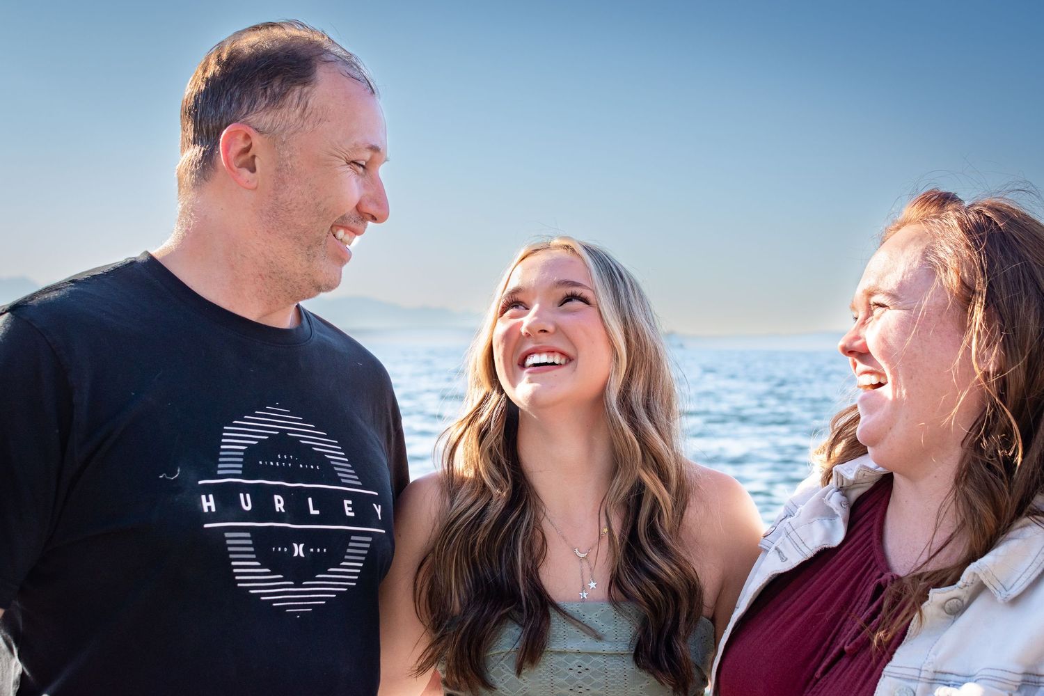 Senior posing with parents at Alki Beach during Seattle graduation photo session.