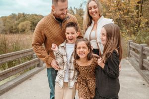 Joyful family of five with three children laugh together on wooden bridge during fall family photo session.