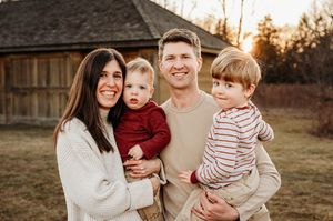 Happy family of four smiling together at golden hour near a barn.