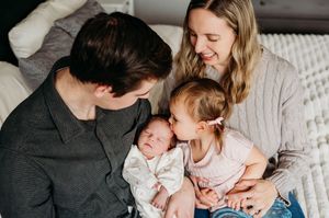 Parents and toddler girl lovingly admiring their sleeping newborn baby indoors.