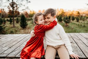 Young siblings hugging on a wooden deck at a Christmas tree farm.