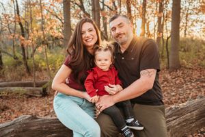 Happy family of three posing on a log in autumn woods with golden fall foliage background.