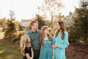 A happy family of four smiles together outdoors at golden hour among evergreen trees.