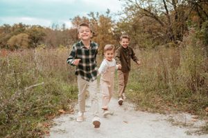 Three energetic young boys run down a nature trail through autumn meadow during outdoor family photo session.