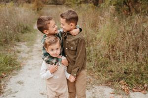 Three brothers share a sweet hug on a rustic path surrounded by colorful fall foliage outdoors.