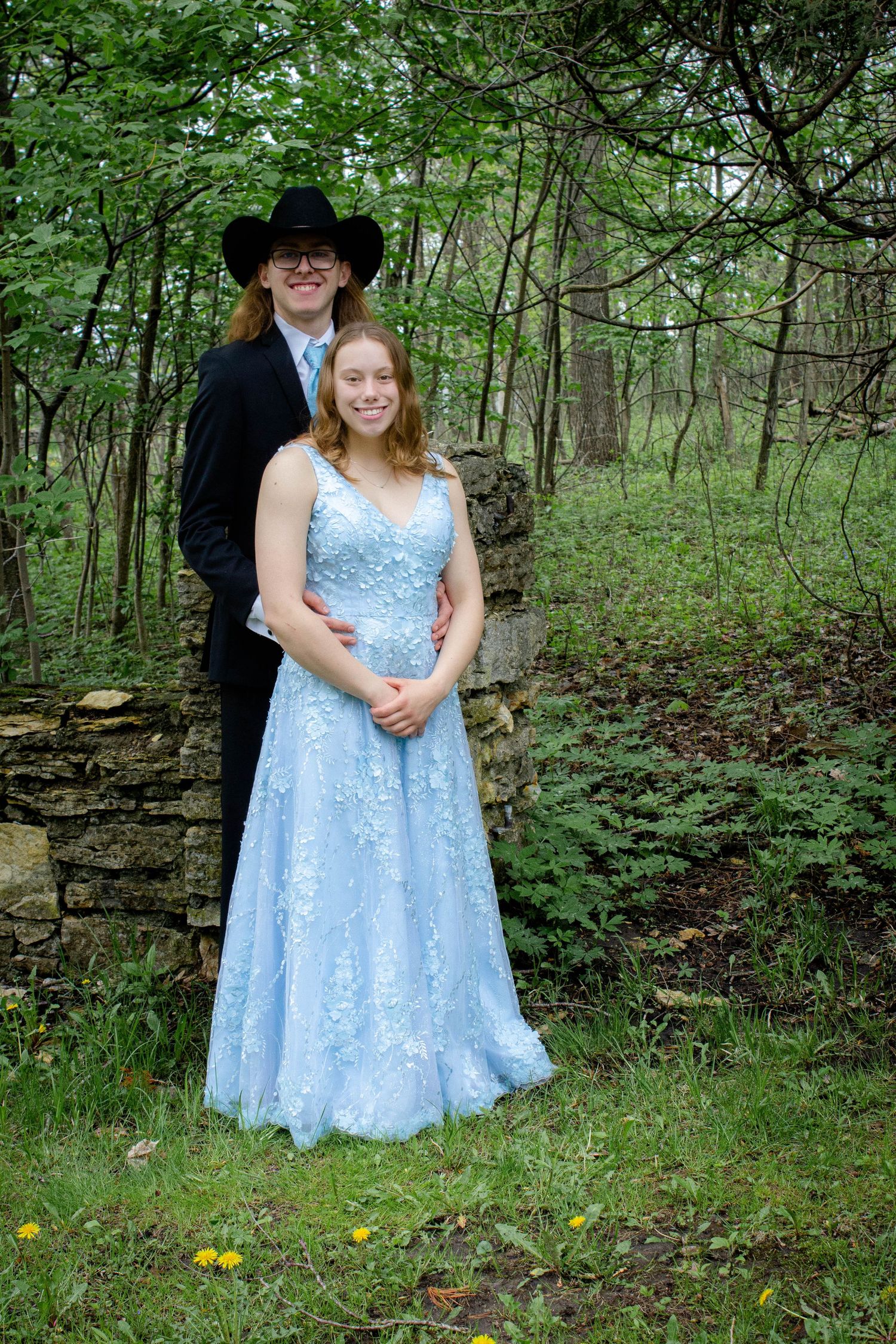 A formal portrait in a wooded setting featuring elegant attire and a blue gown.