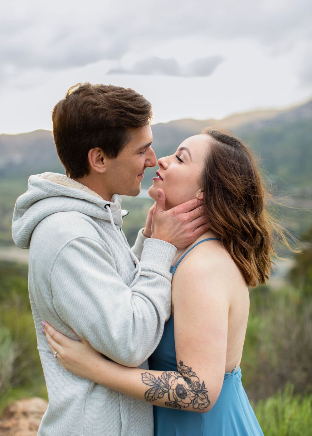 Romantic couple embracing on a mountain overlook with rolling hills in the background.