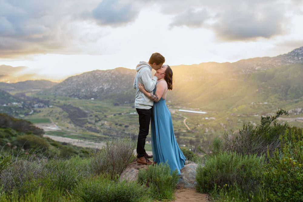 Couple sharing romantic sunset moment on mountain trail overlooking valley below.