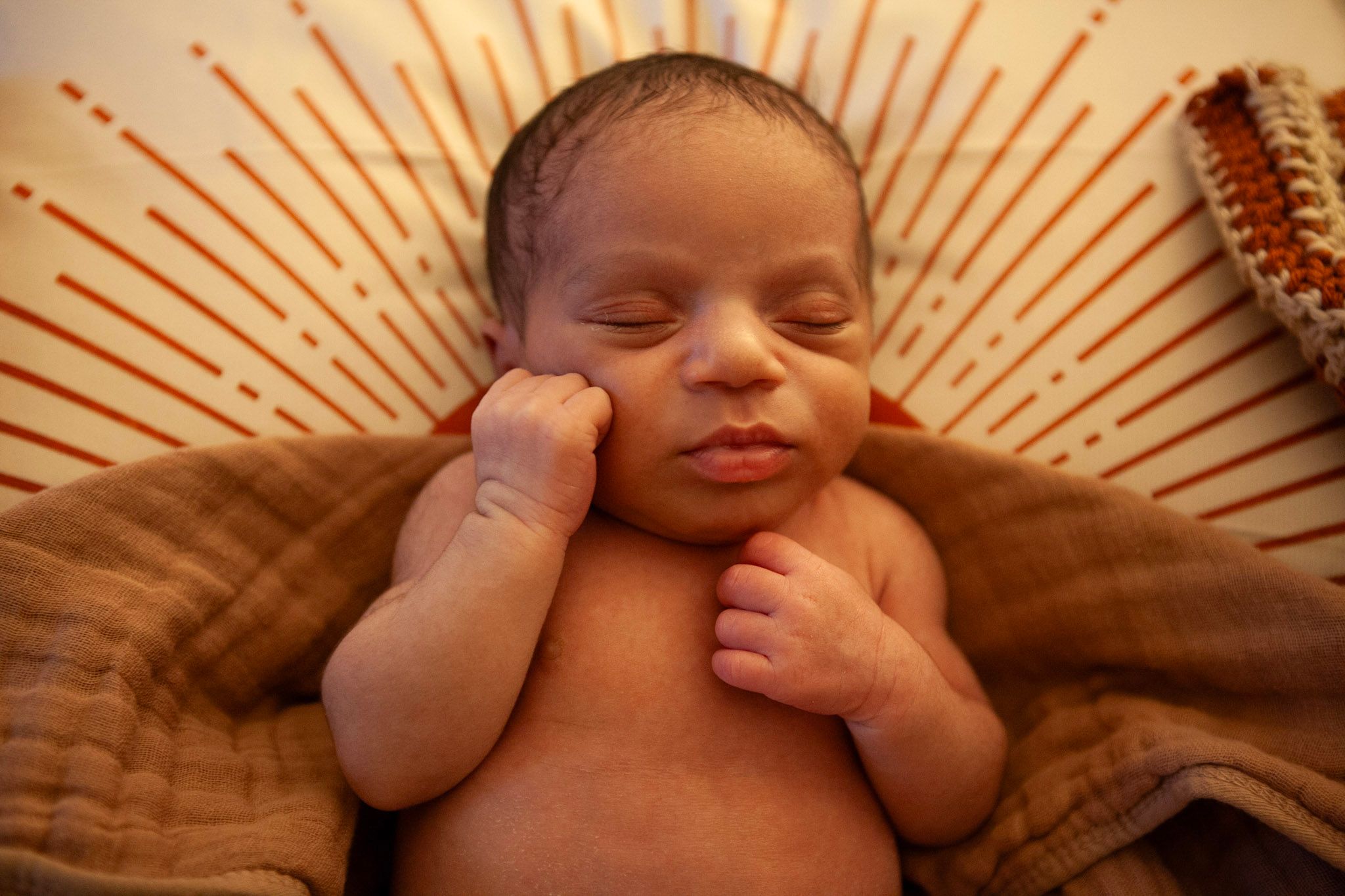Sleeping newborn baby resting on a textured brown blanket with radiating pattern backdrop.