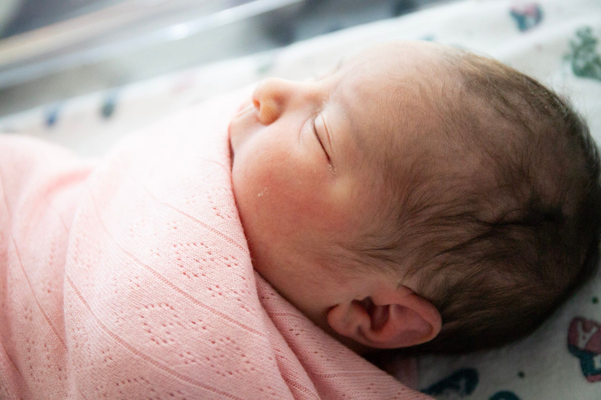 Peaceful newborn baby swaddled in pink blanket resting on hospital bedding.