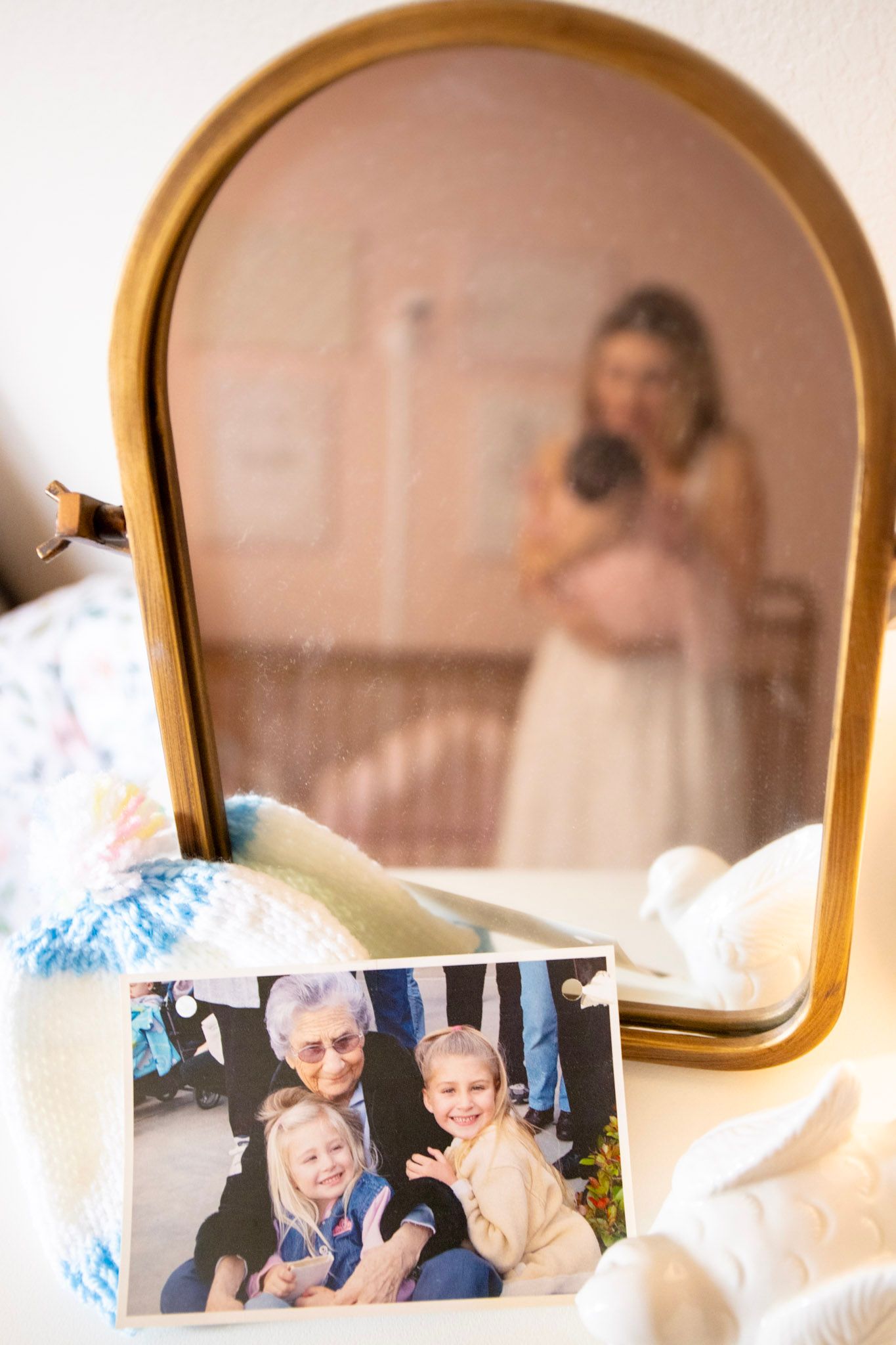 A vintage gold mirror reflects a pregnant woman as a cherished family photo of grandma and two children rests in the foreground.