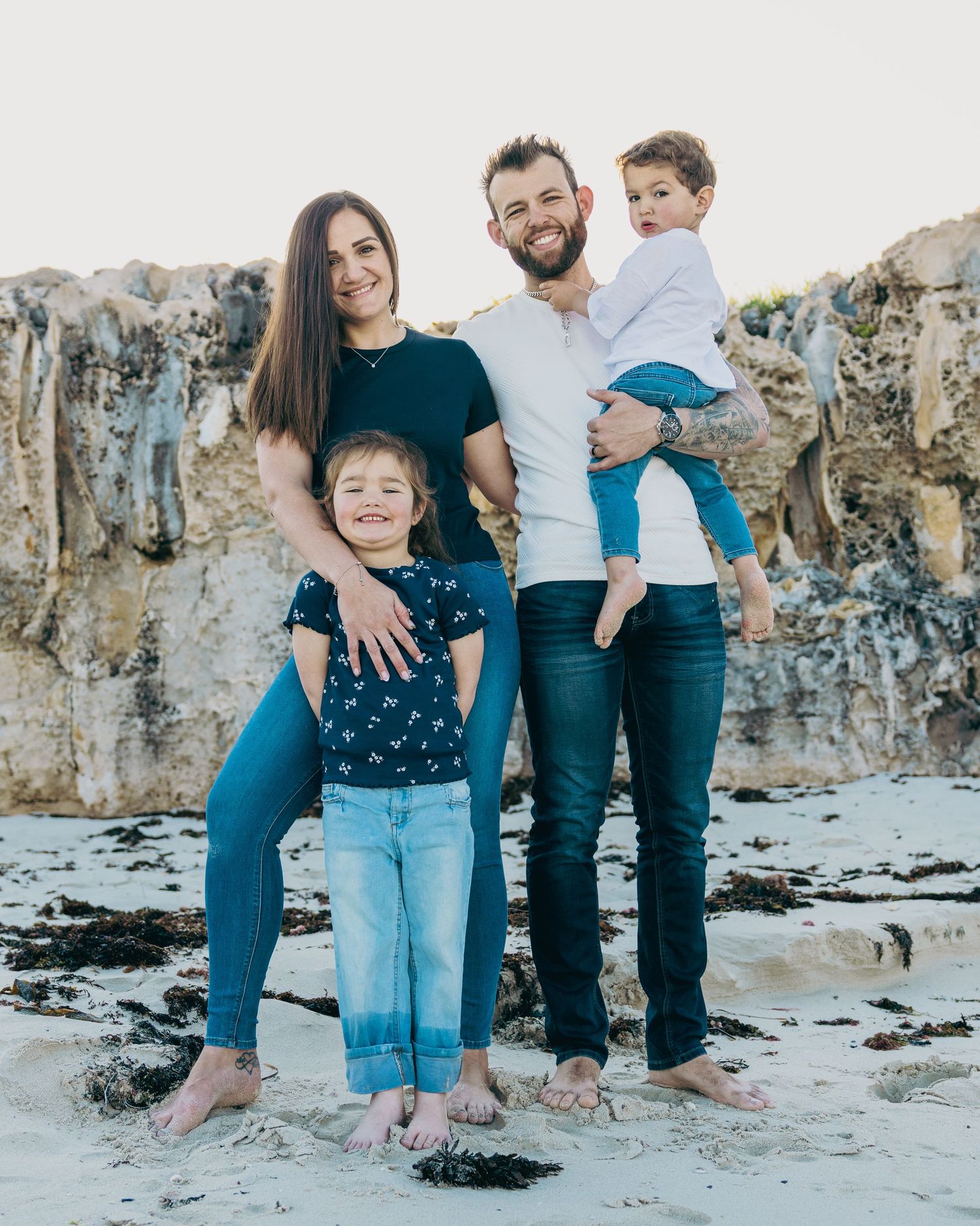 Casual family photoshoot on a rocky beach with everyone wearing coordinated blue outfits.
