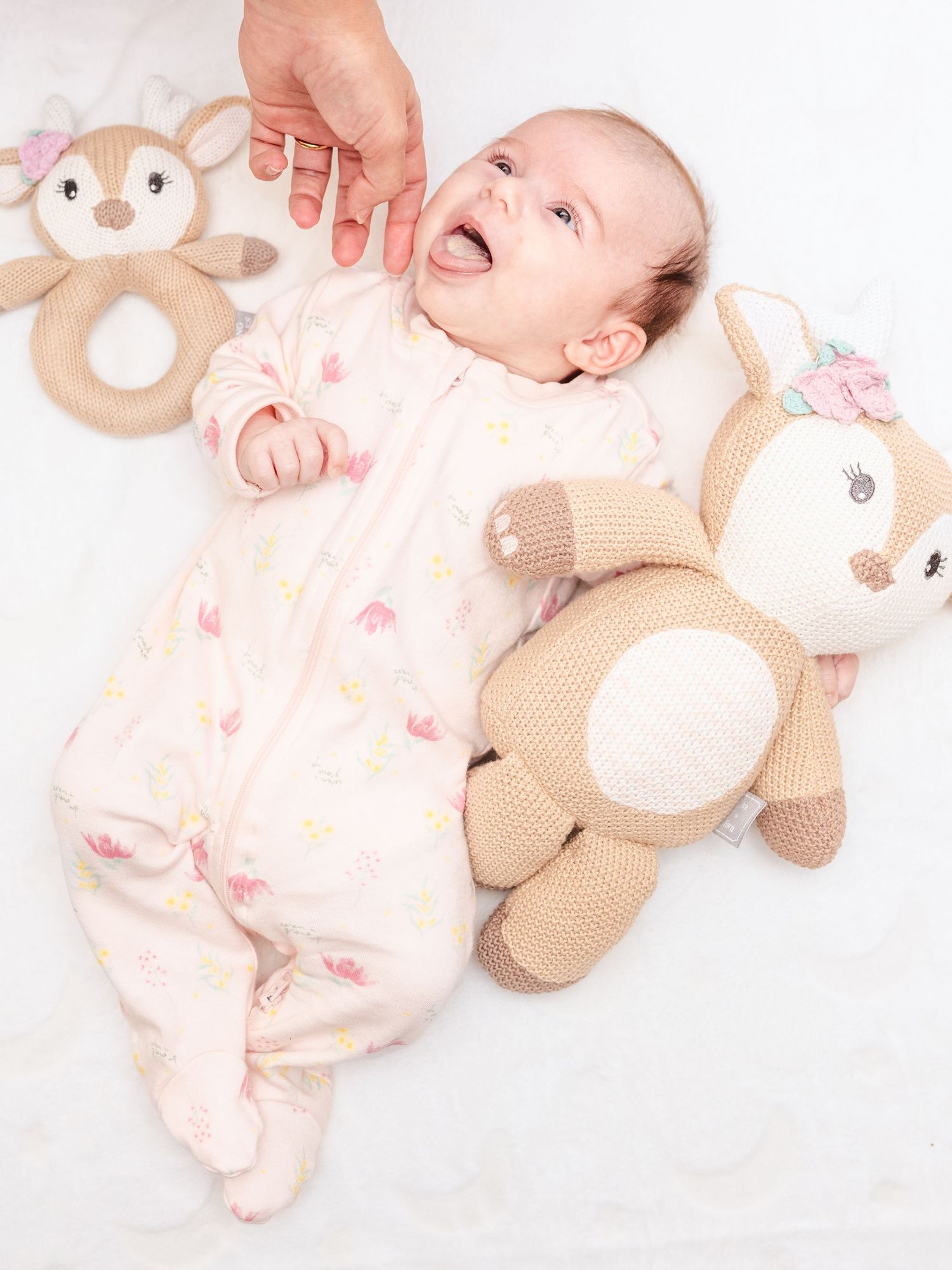 Baby lying on white blanket surrounded by plush animal toys.