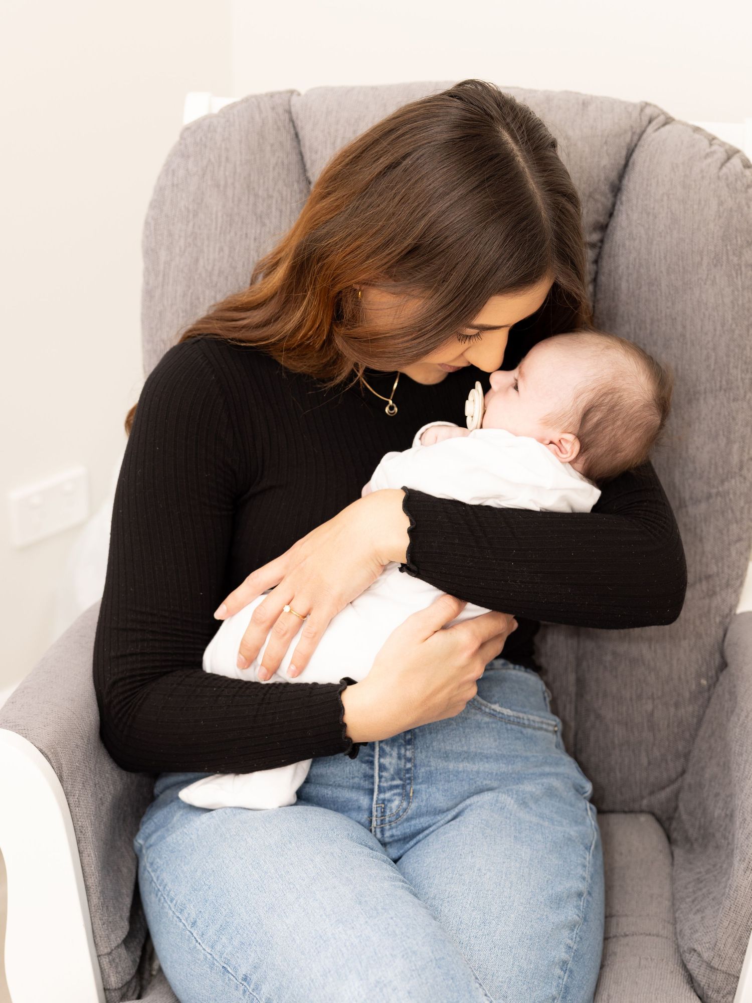 Tender moment shared between parent and infant in gray armchair.