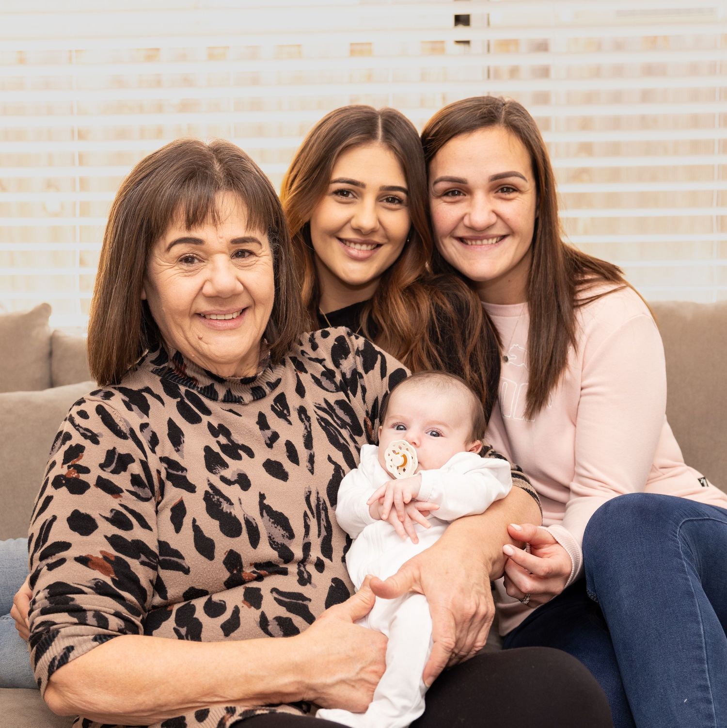 Multi-generational family gathering with infant on cozy sofa.