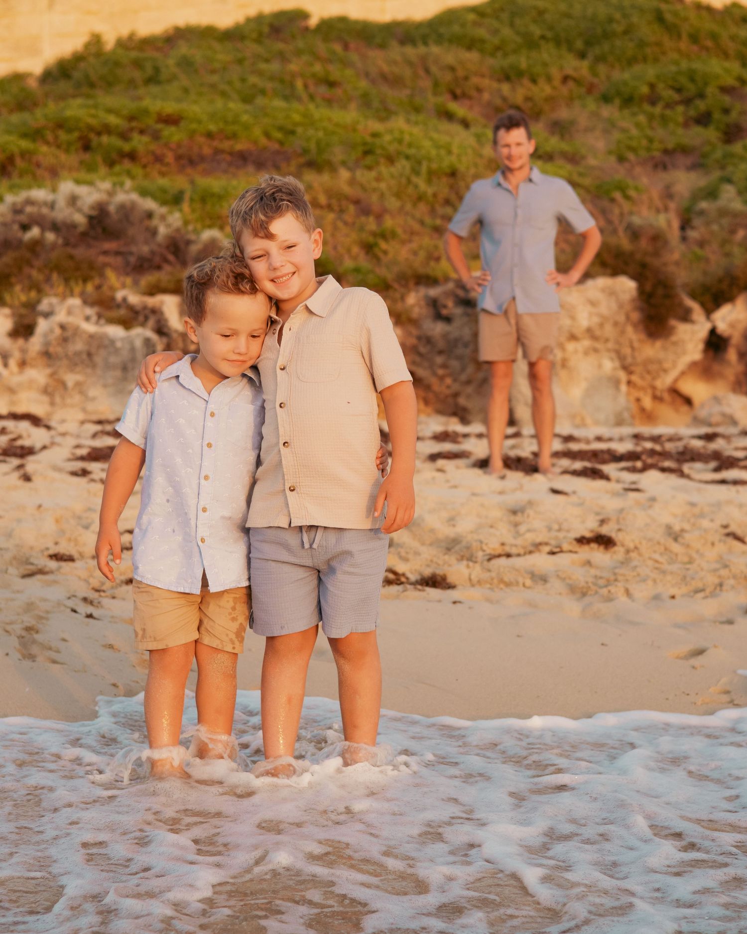 People walking together on a sandy beach with coastal cliffs and golden sunlight in the background.