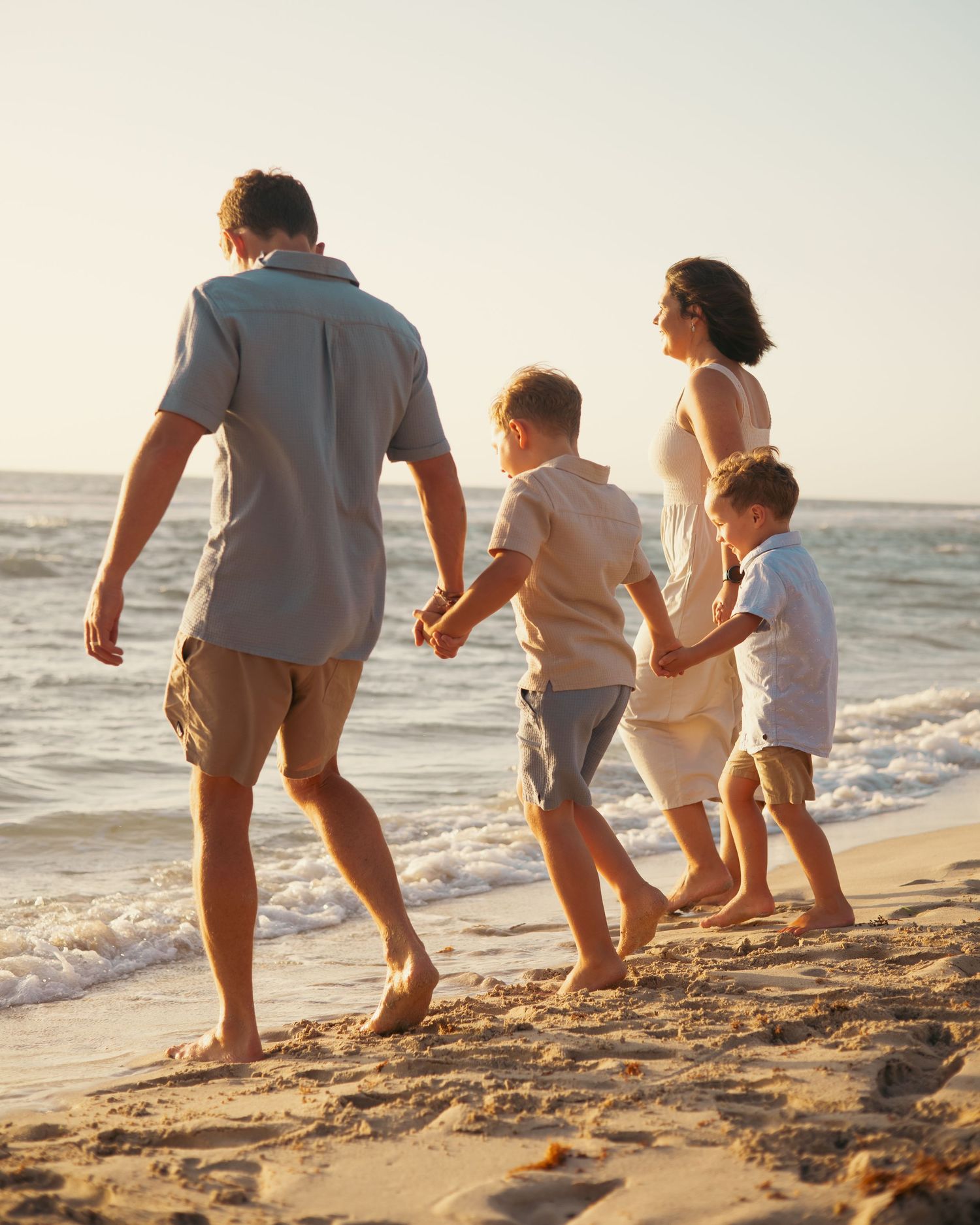 Family members walking barefoot along the sandy beach at sunset.