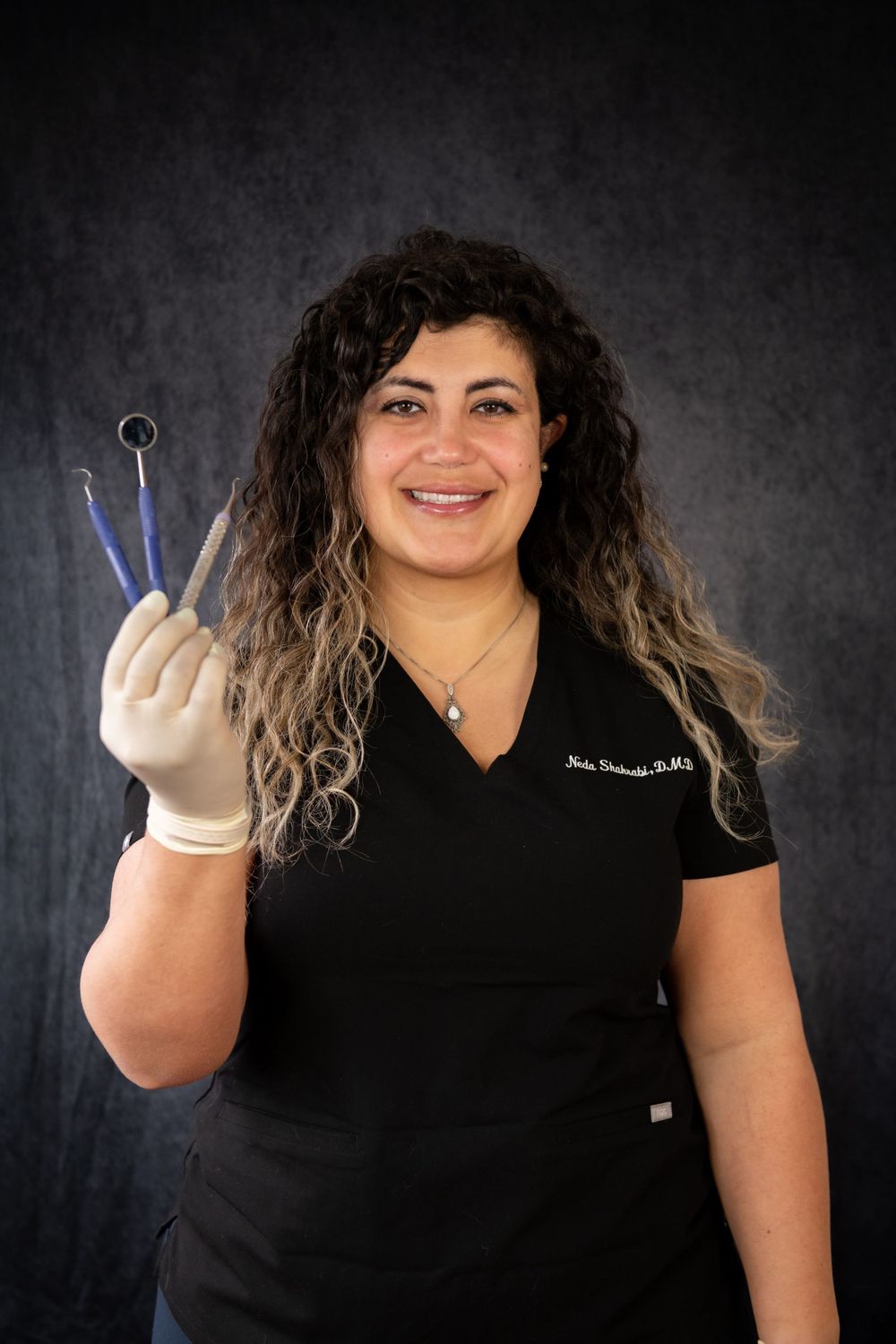Dental professional in black scrubs holding dental tools while wearing protective gloves.