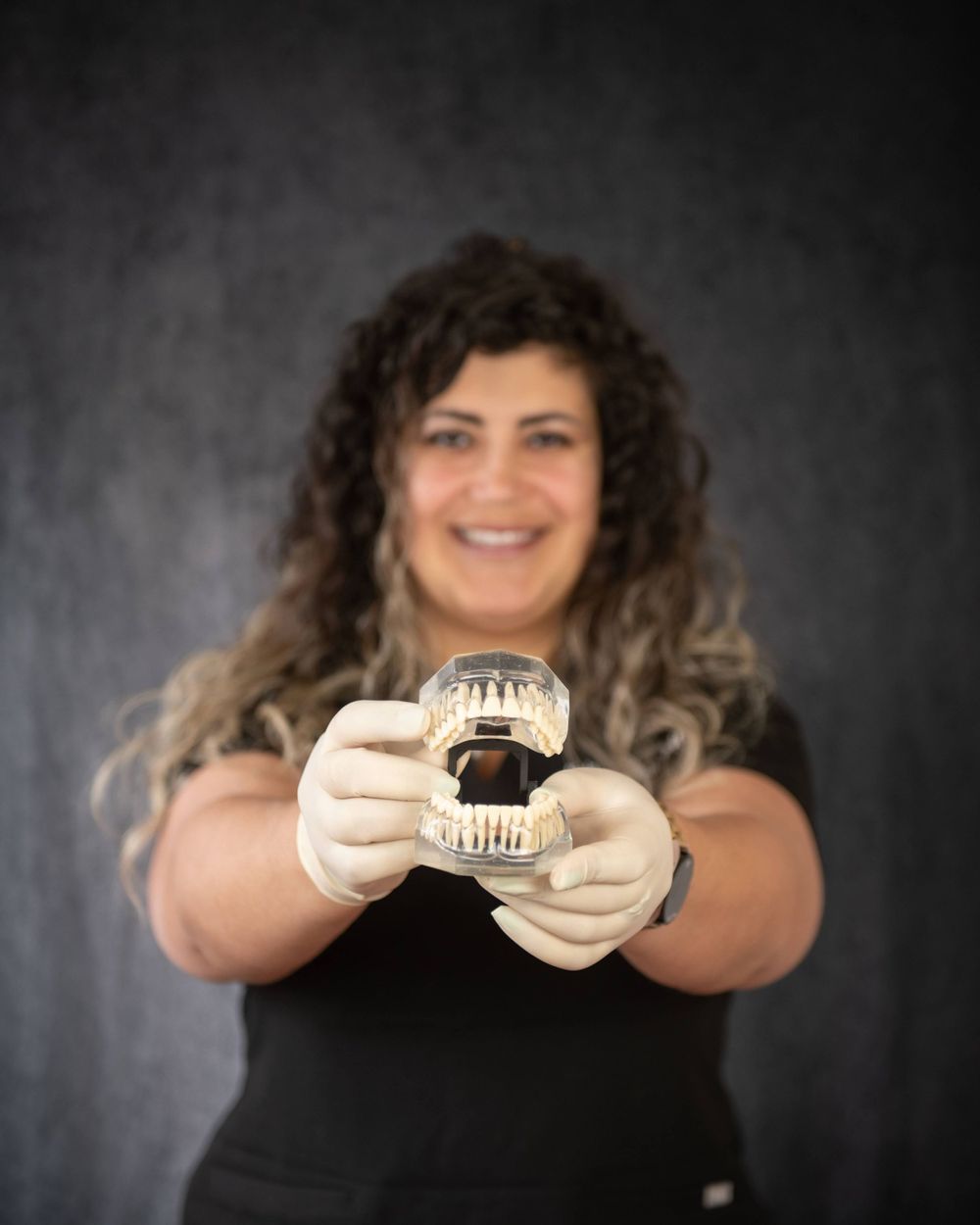 A dental professional wearing a black top holds up a dental model demonstrating teeth structure against a dark background.