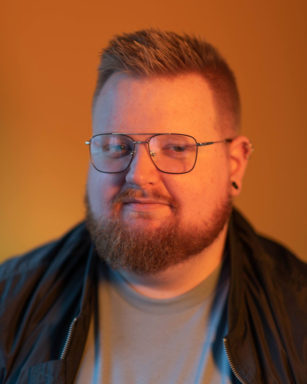 Studio portrait with warm lighting wearing casual attire and glasses.