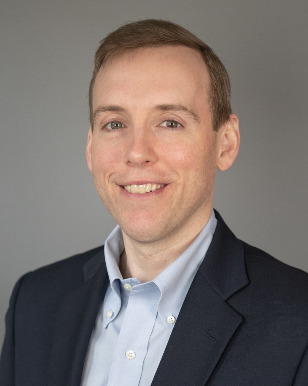 Corporate headshot of person in navy suit and light blue button-down shirt.