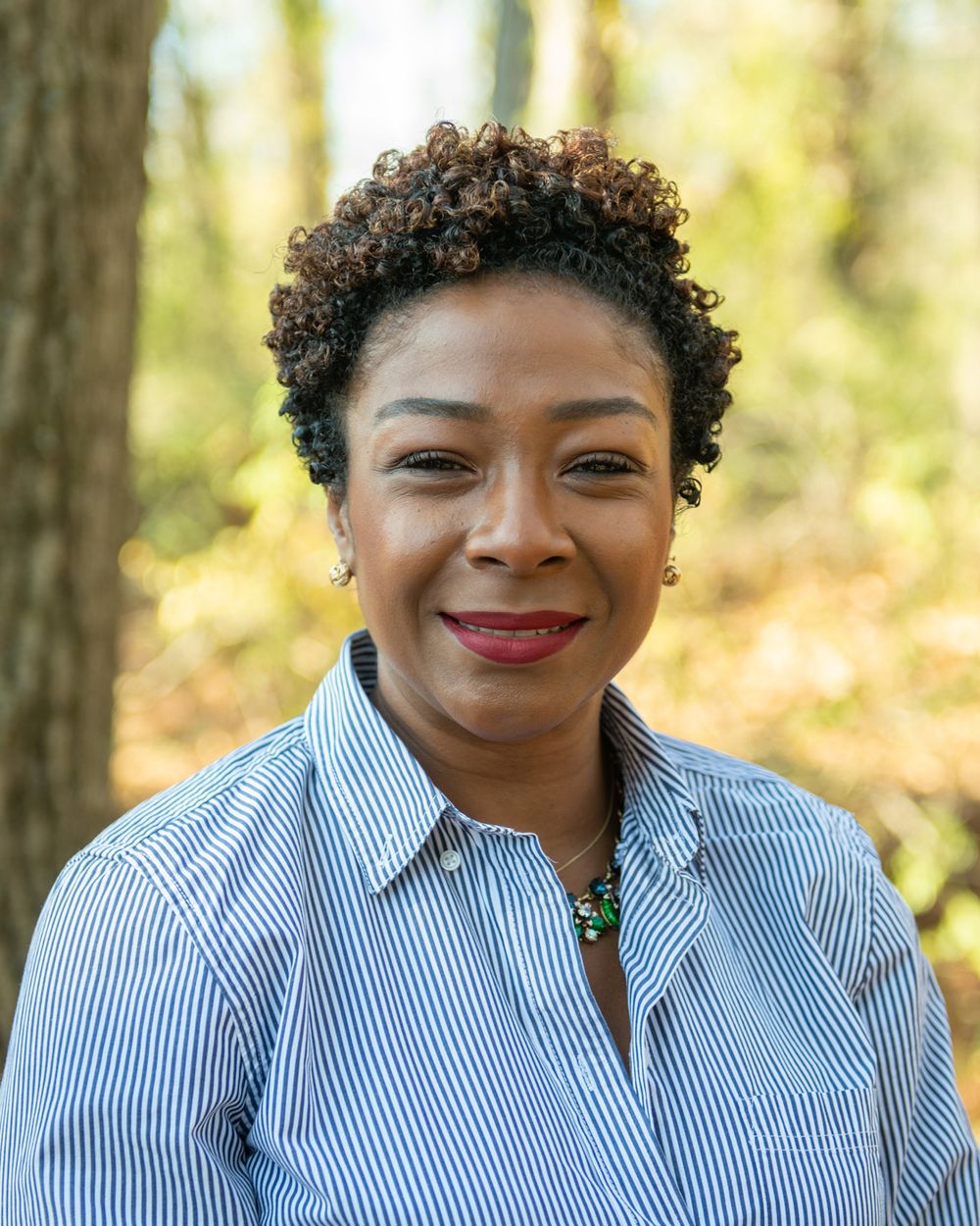 Professional portrait outdoors with autumn trees in background.