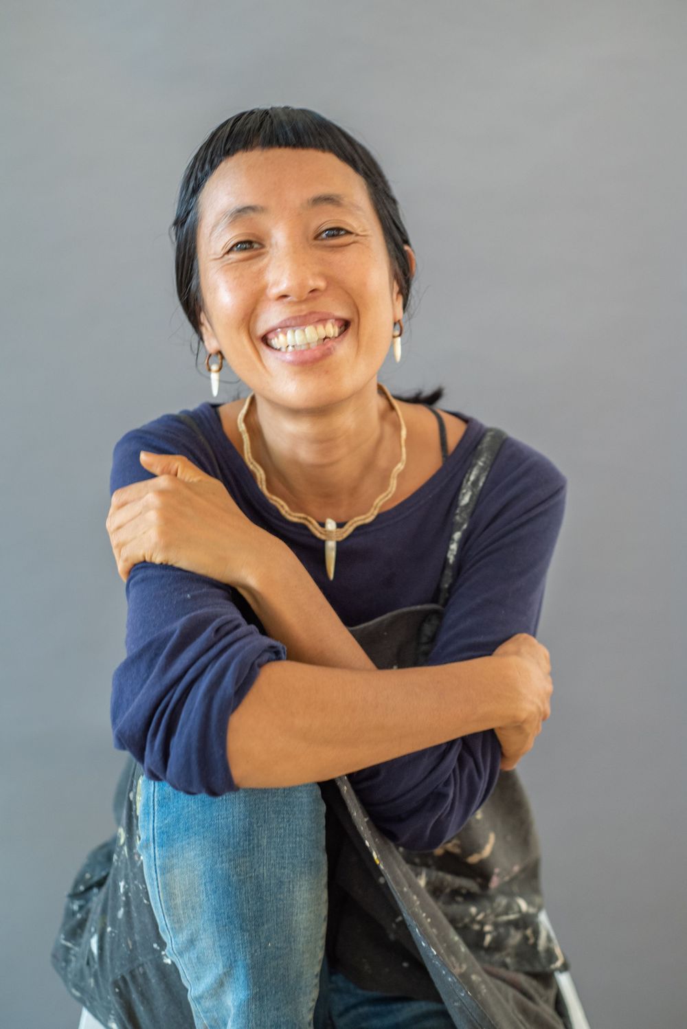 A candid portrait showing someone in navy blue clothing hugging their knees and smiling warmly.