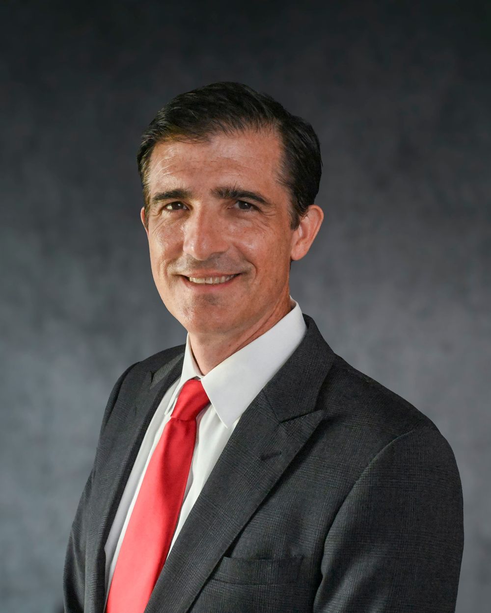 Professional headshot of someone in a dark suit and bright red tie against a gray backdrop.