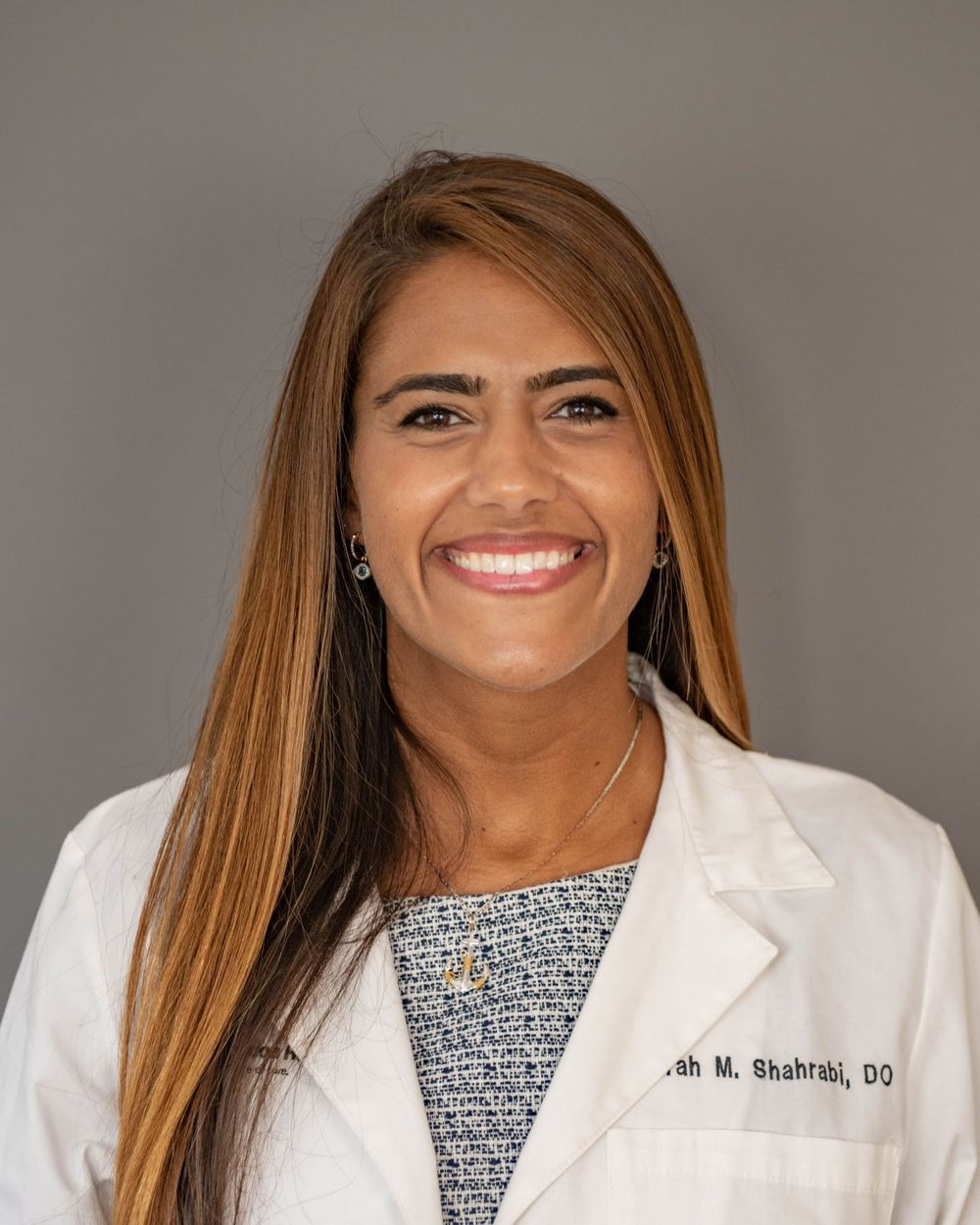 Medical professional wearing a white coat and patterned blouse smiling at the camera.
