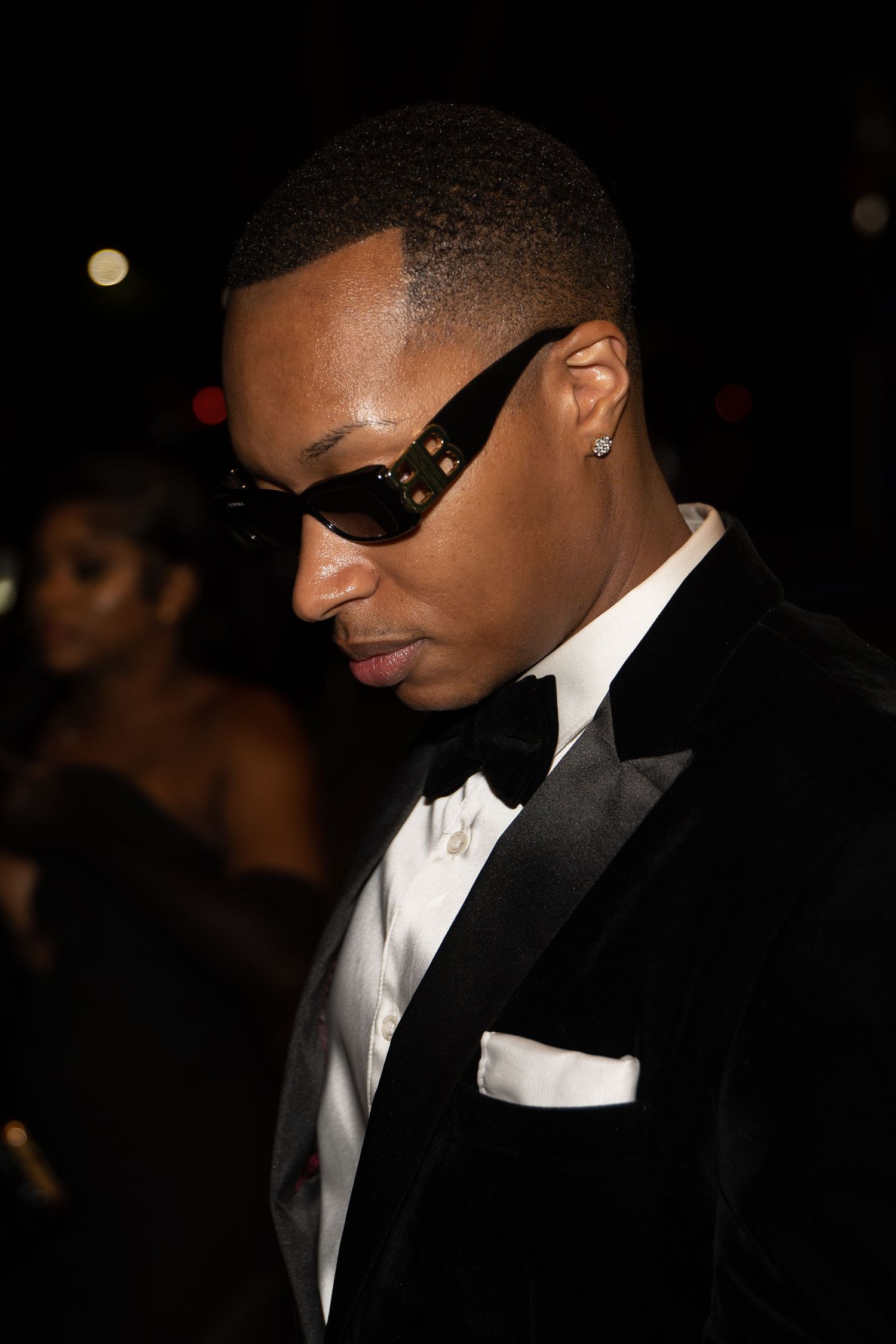 A person in a black tuxedo and white dress shirt wearing dark sunglasses at a formal event.