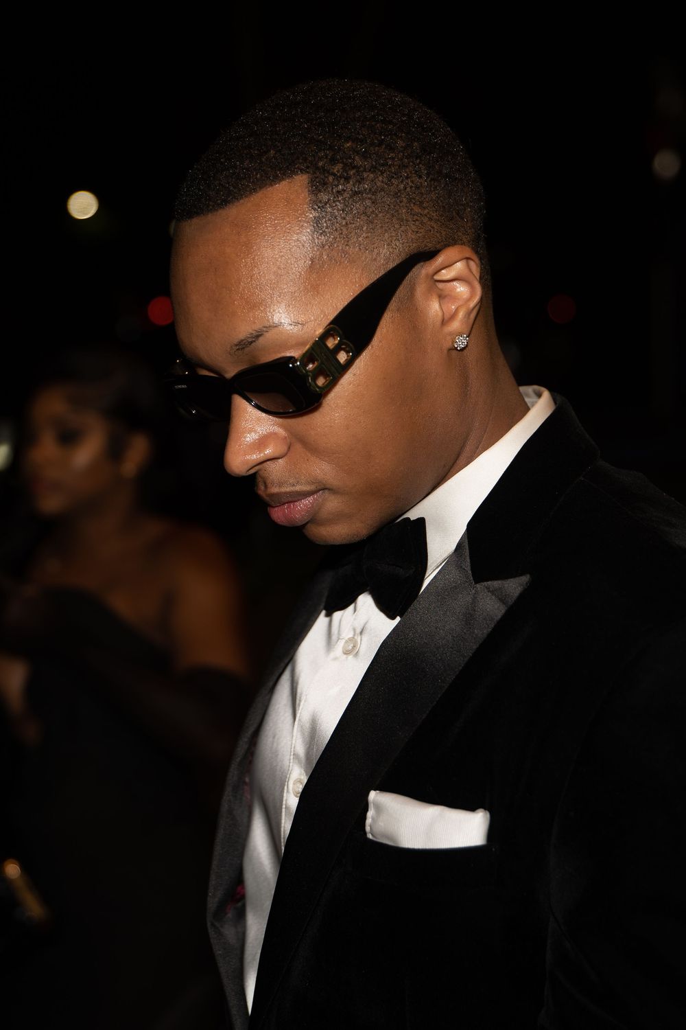 A person in a black tuxedo and white dress shirt wearing dark sunglasses at a formal event.