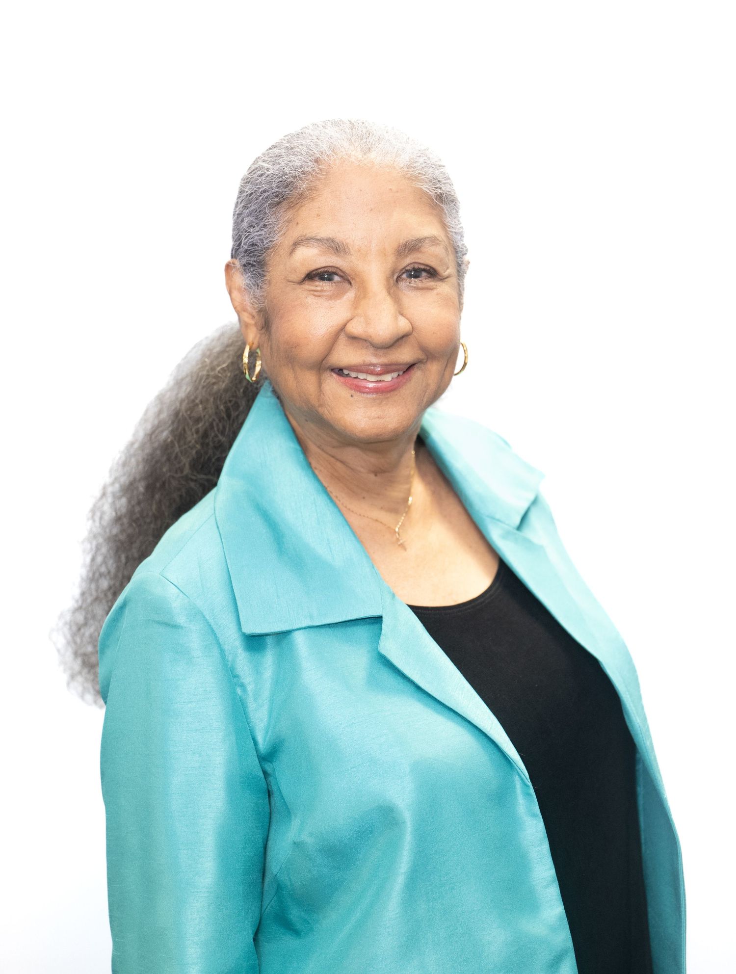 Elegant woman wearing turquoise blazer and black top smiles warmly against white background.