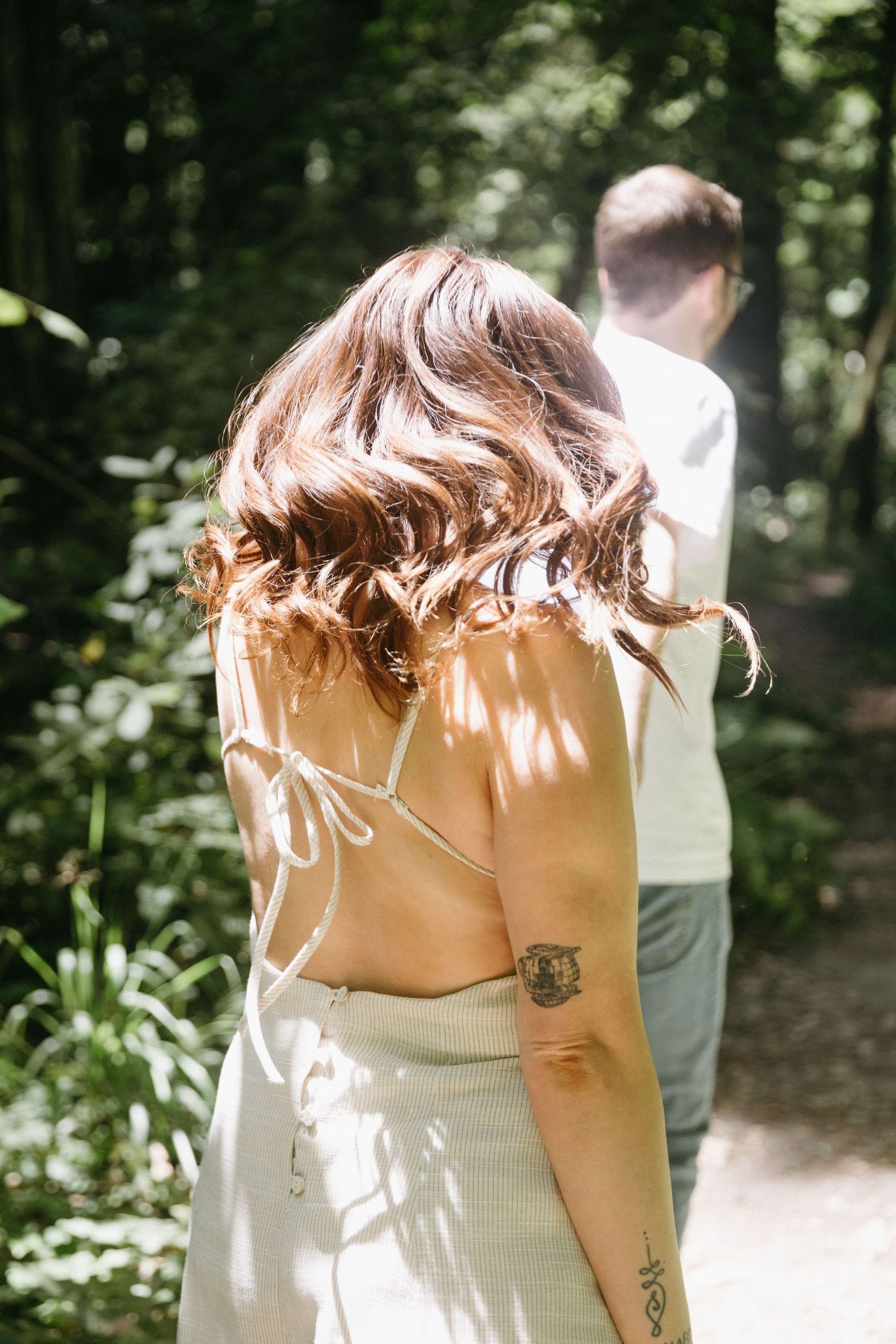 Back view of person in white dress with tattoos standing on forest trail.