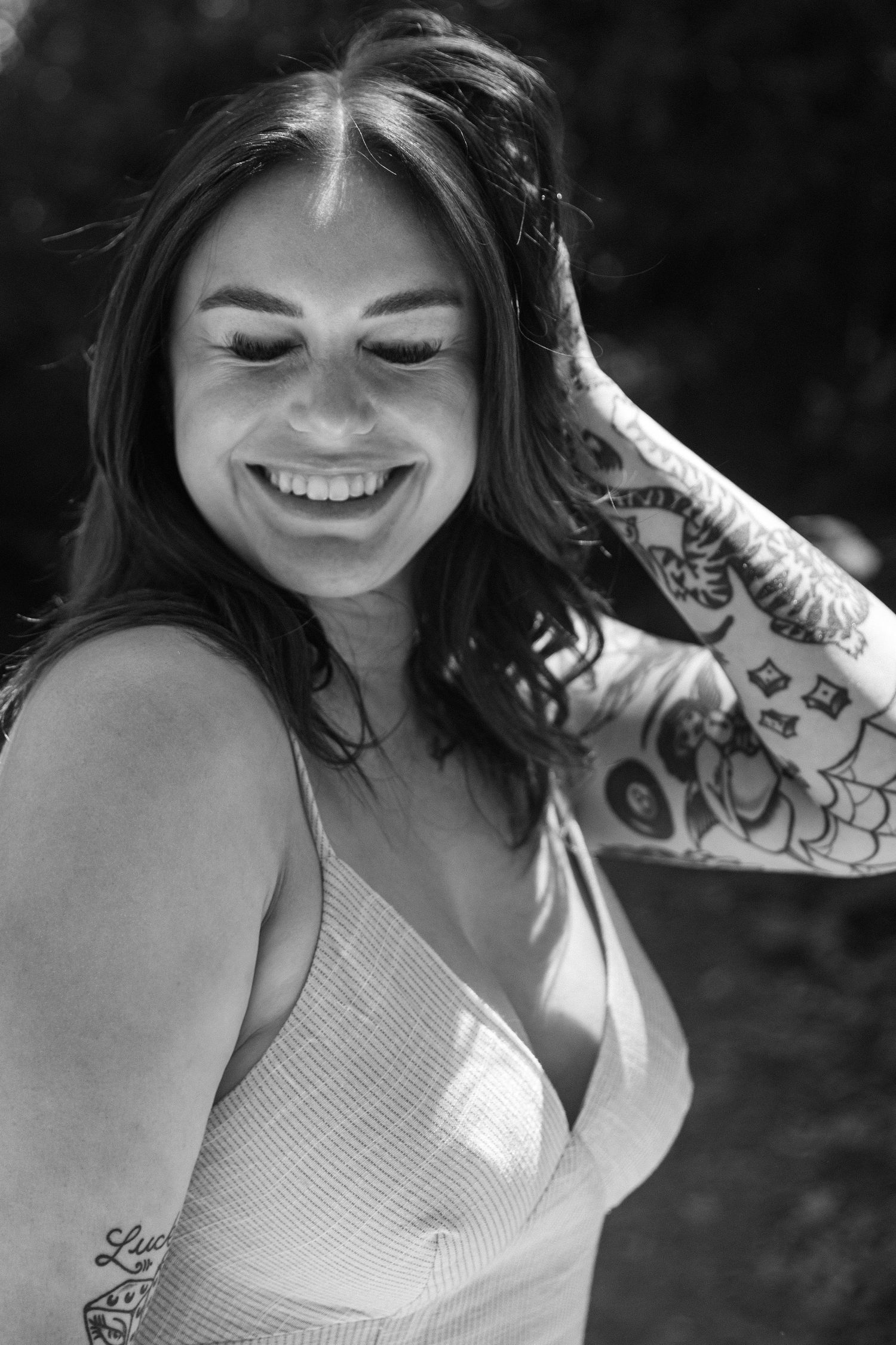 Black and white portrait of smiling woman in white dress with visible tattoos outdoors.