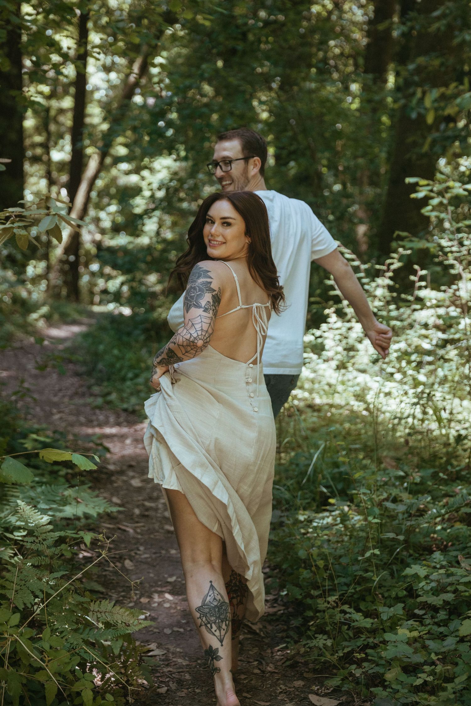 Couple enjoying a playful moment on a forest trail in summer sunlight.