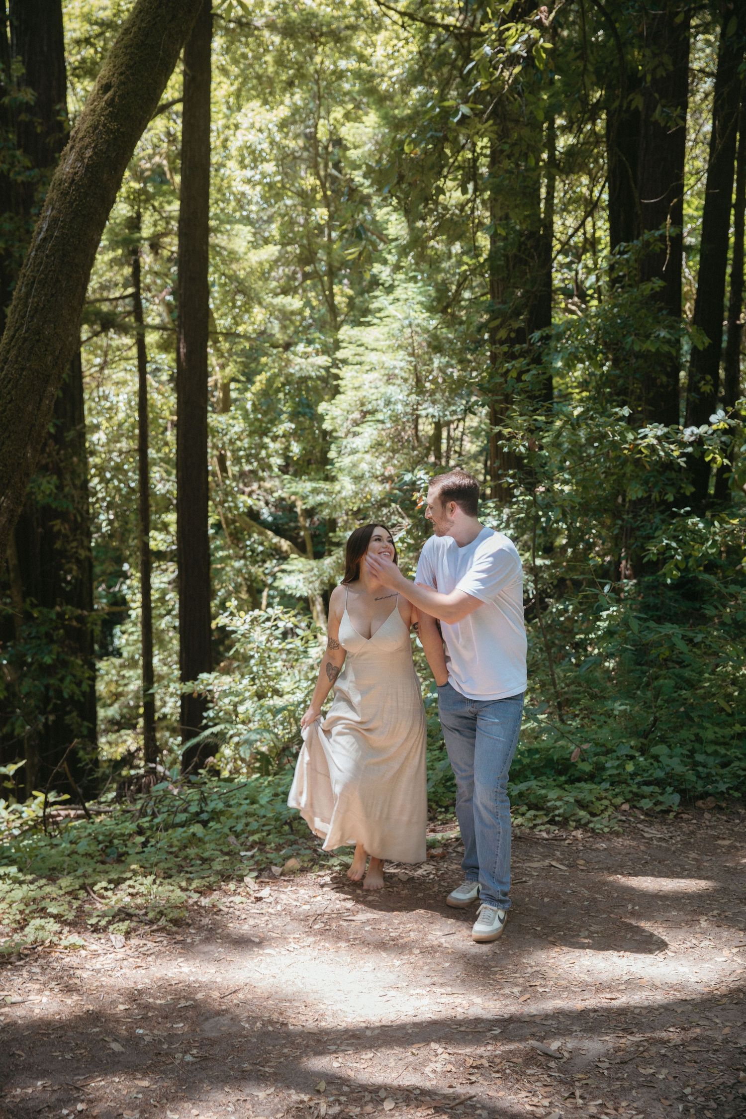 Couple laughing together while walking on sunlit forest path.