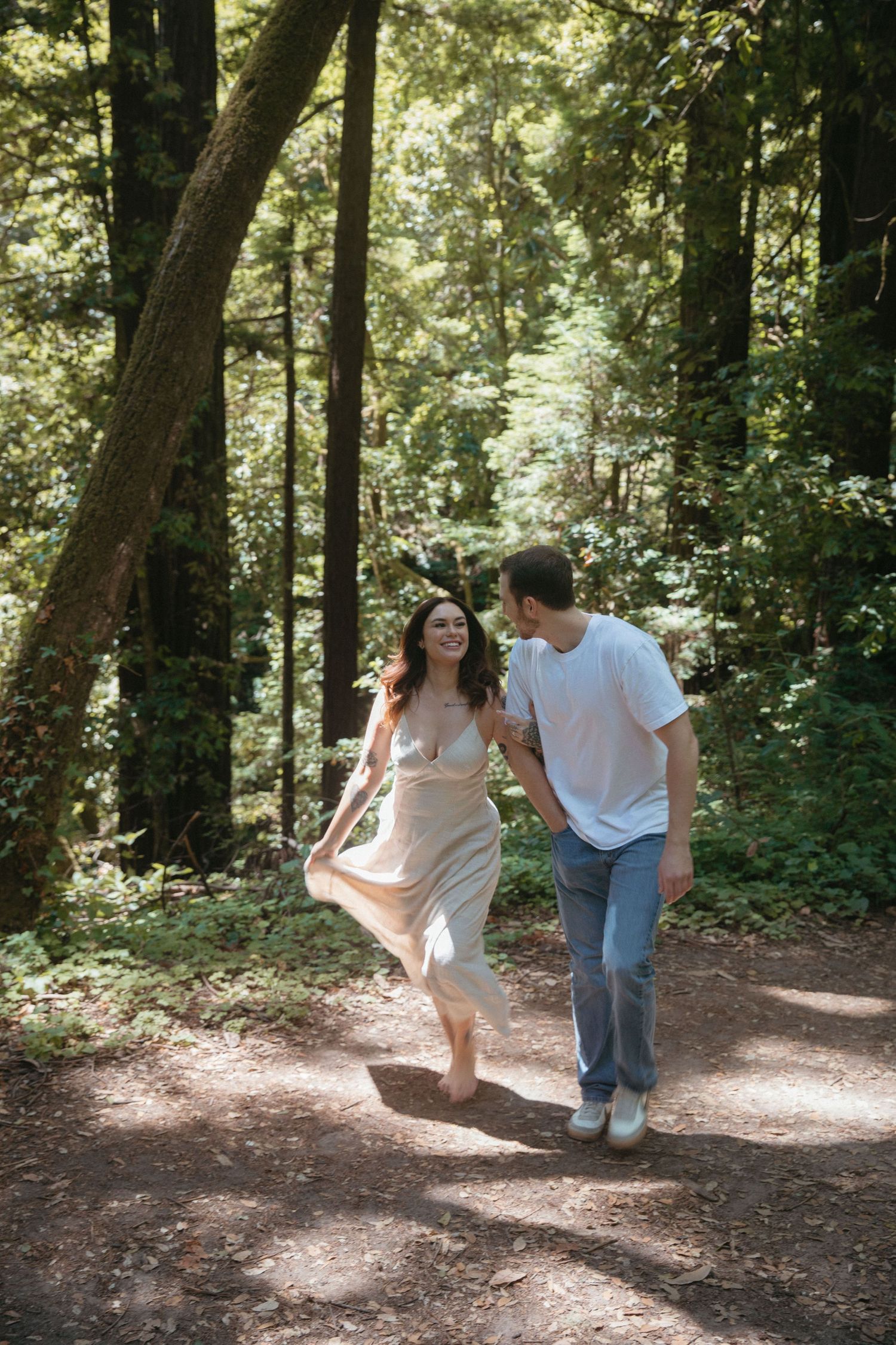 Couple playing and dancing together on forest trail bathed in sunlight.