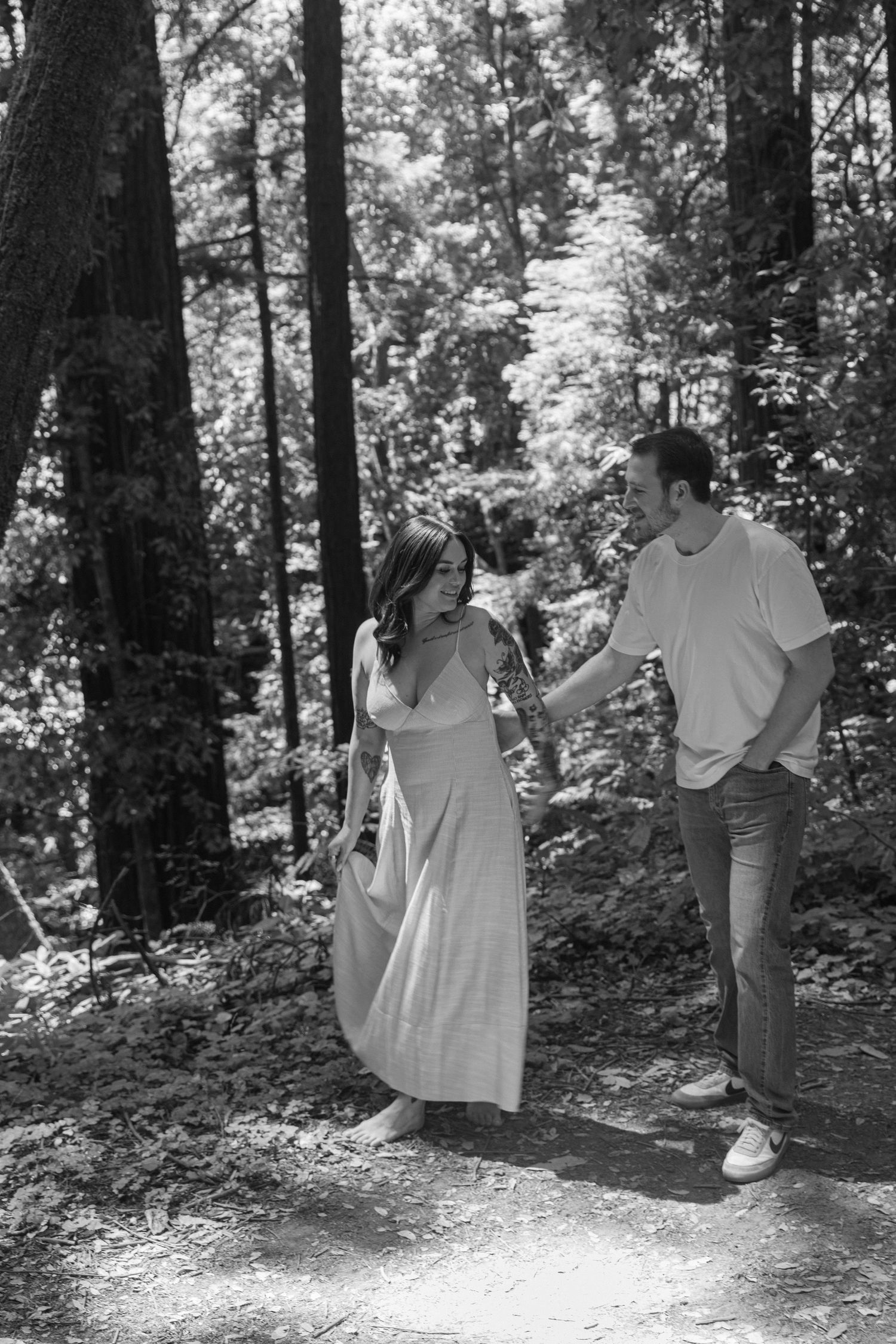 A couple walks hand in hand along a peaceful woodland path in black and white.