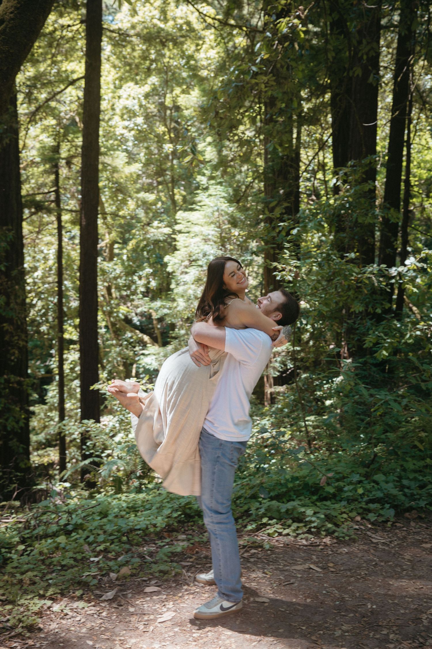 A playful moment captured as a couple embraces in a lush forest setting.