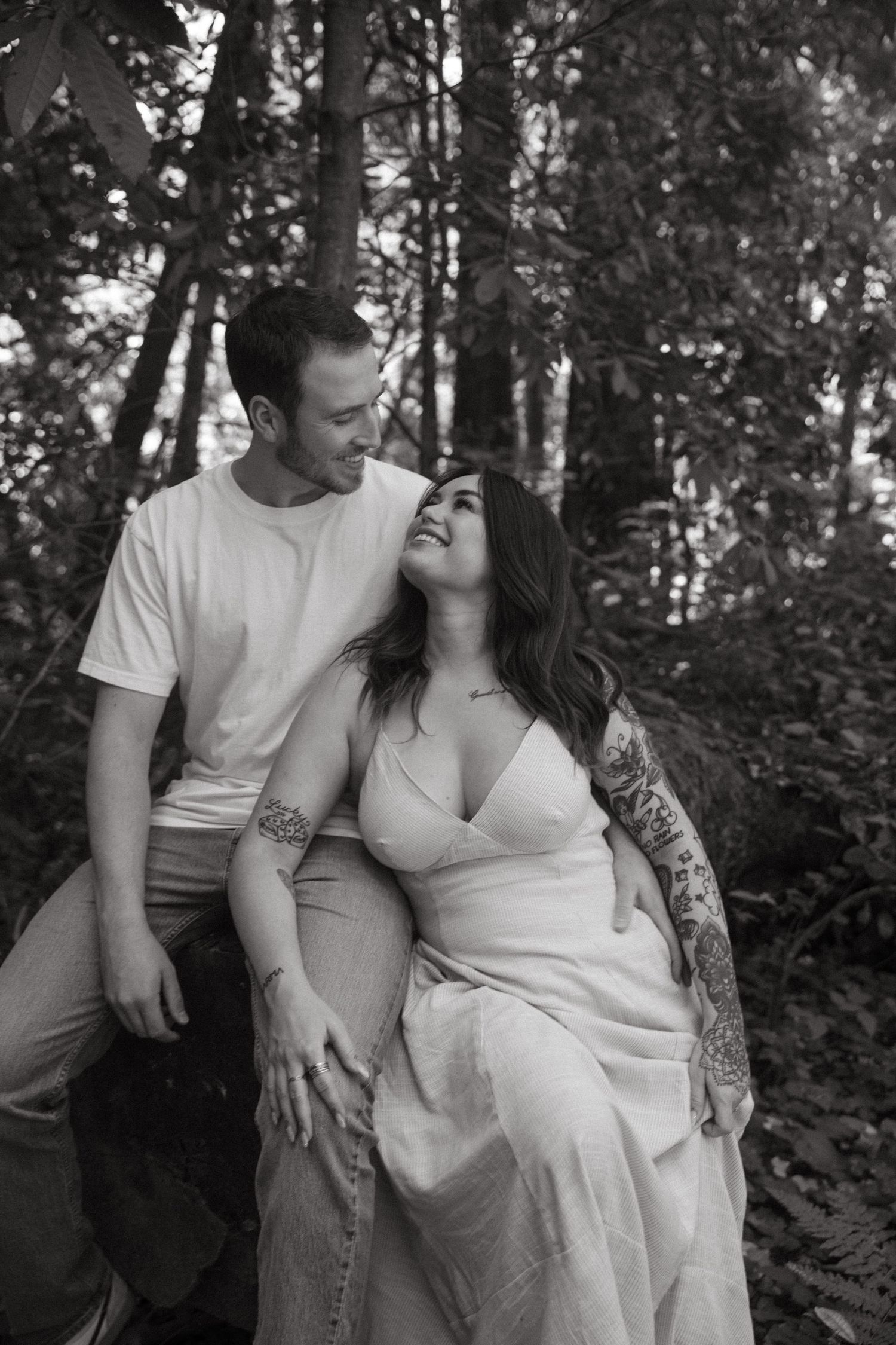An intimate black and white portrait of a couple sharing a tender moment in the woods.