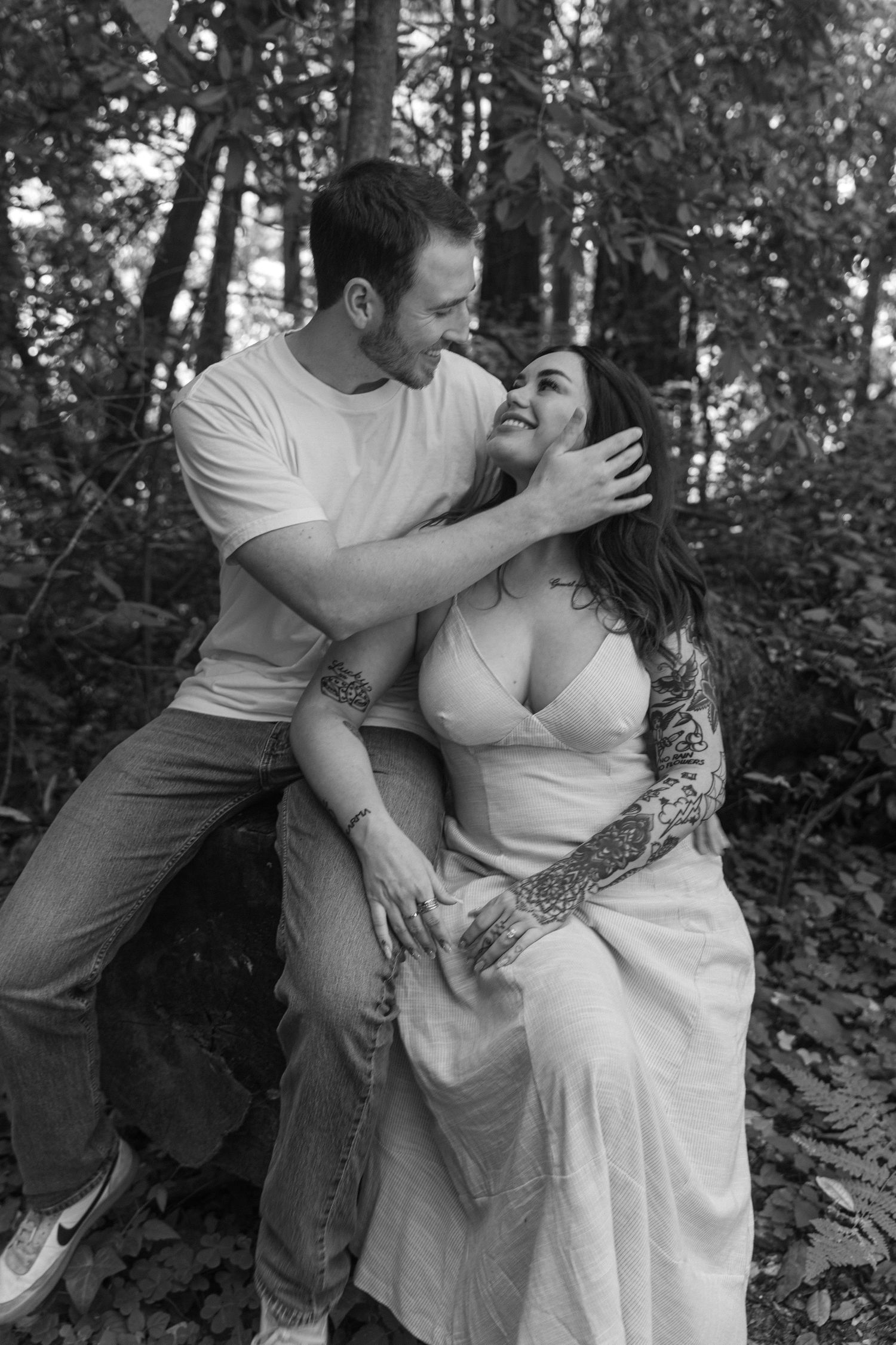 A candid forest photoshoot showing a romantic couple embracing and laughing in black and white.