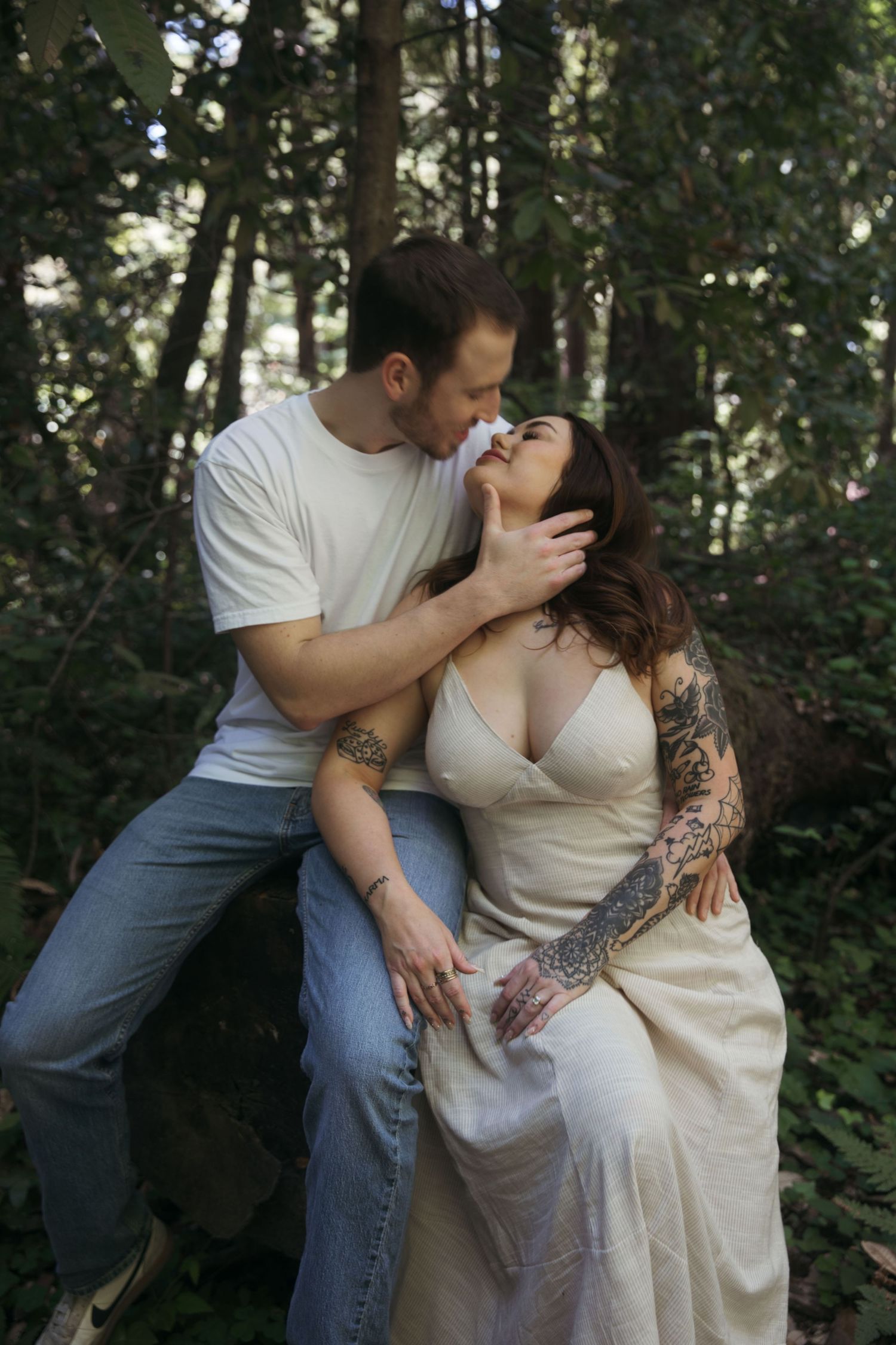 An intimate forest portrait of a couple in light clothing sharing a tender moment.