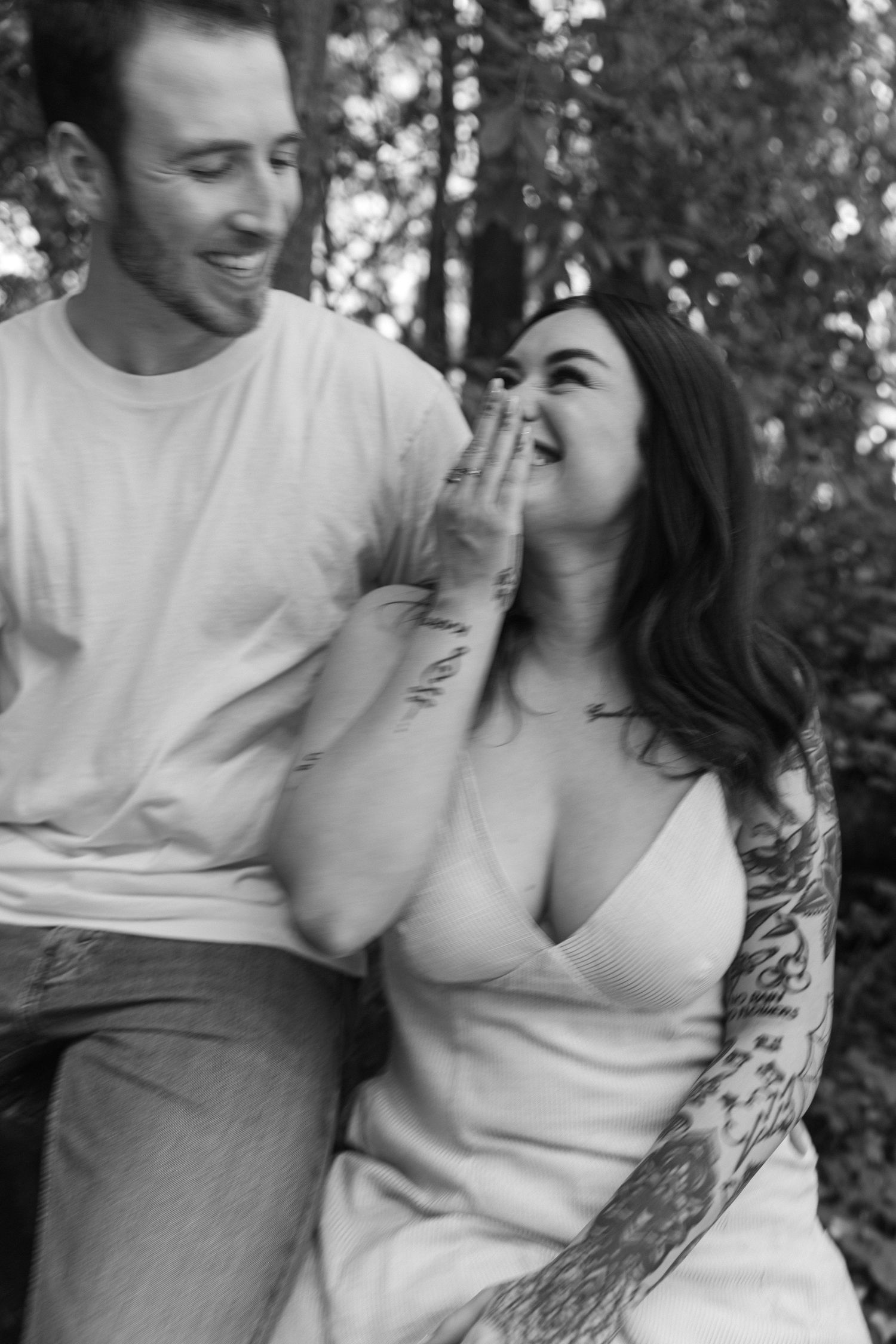 A playful couple sharing laughter during an outdoor photo session in the woods.