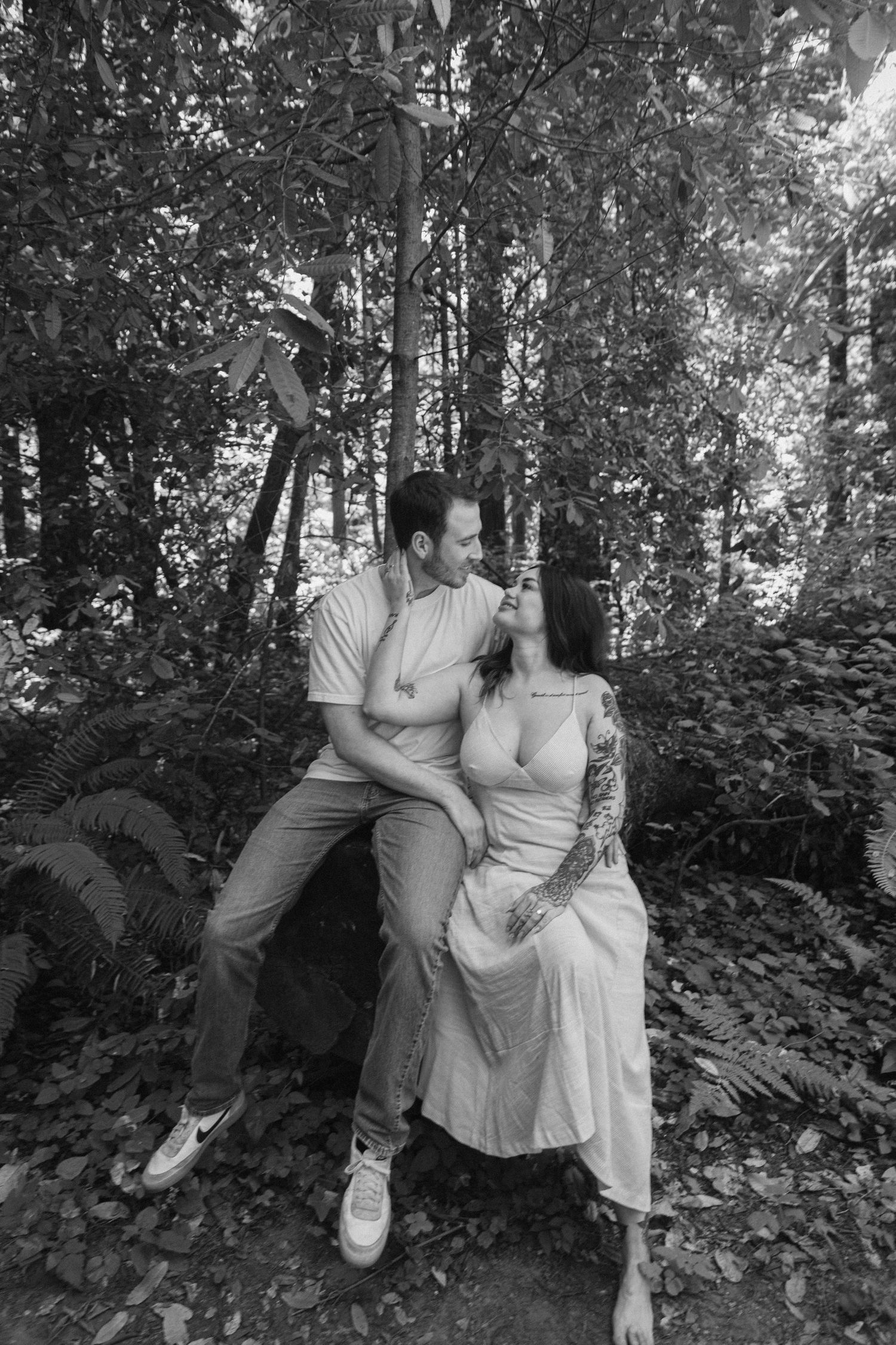 A romantic black and white photo of a couple posing playfully among forest trees.
