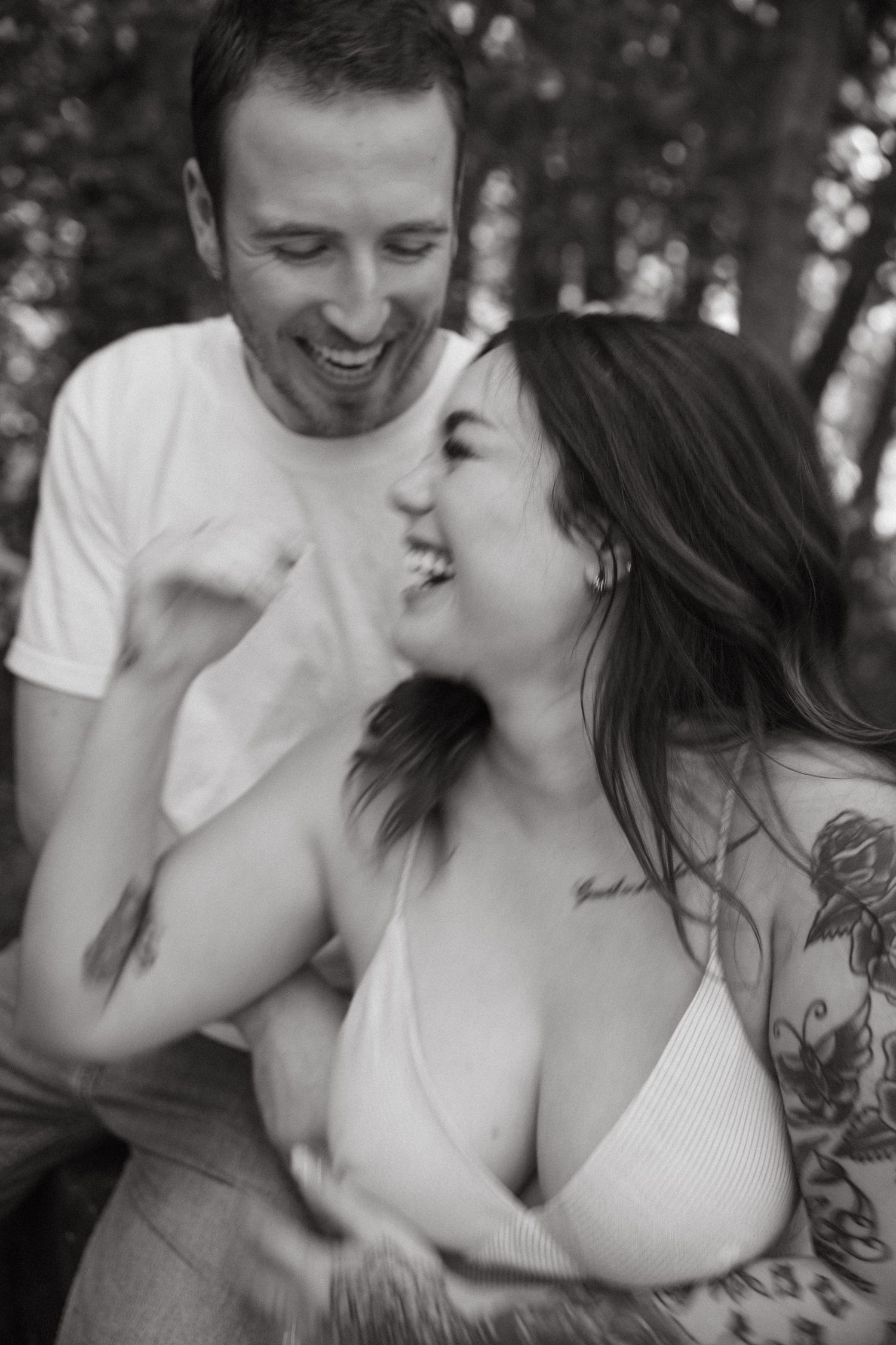 A black and white portrait capturing natural laughter between a couple in the woods.