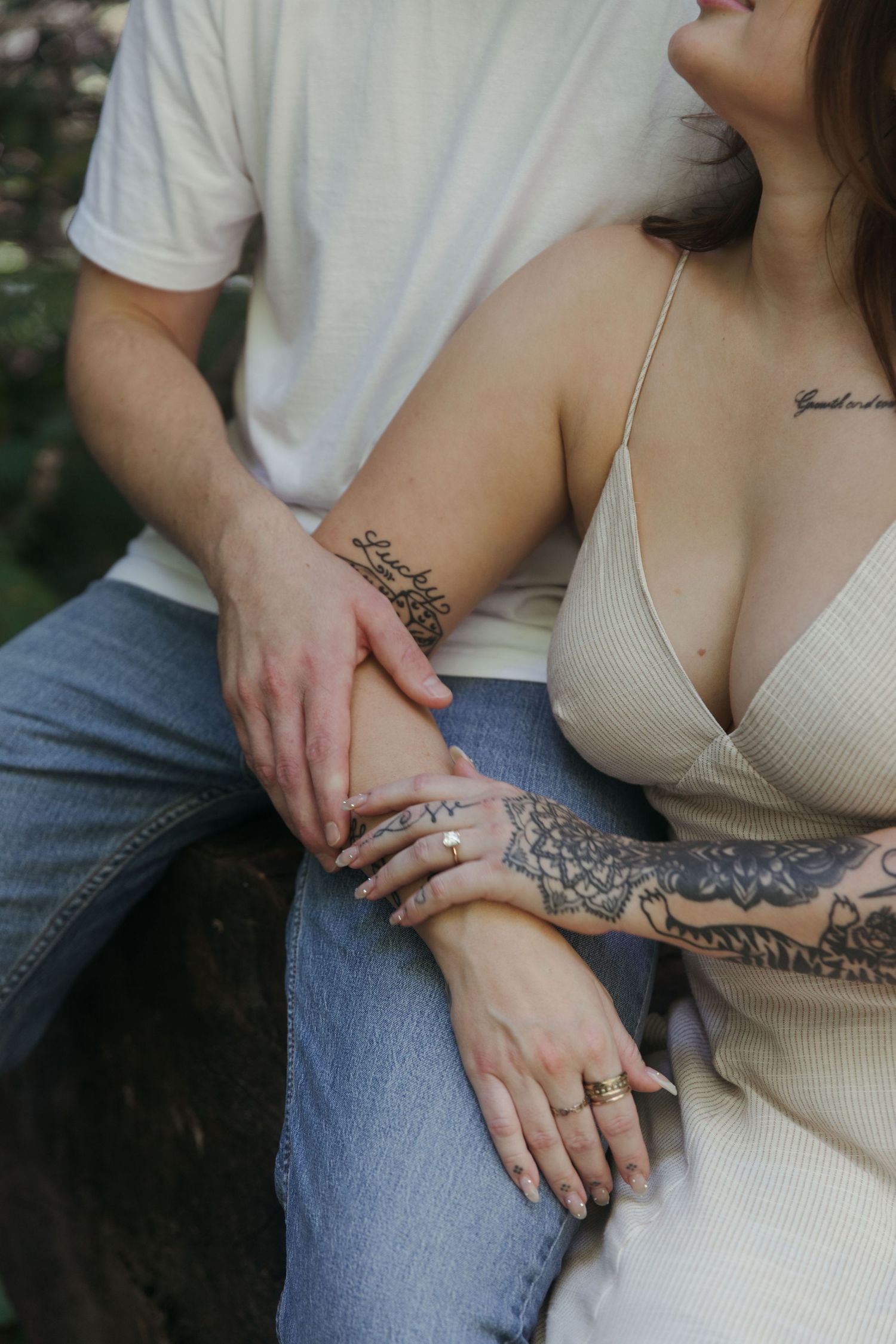 An intimate close-up showing tattooed arms and hands with engagement rings.